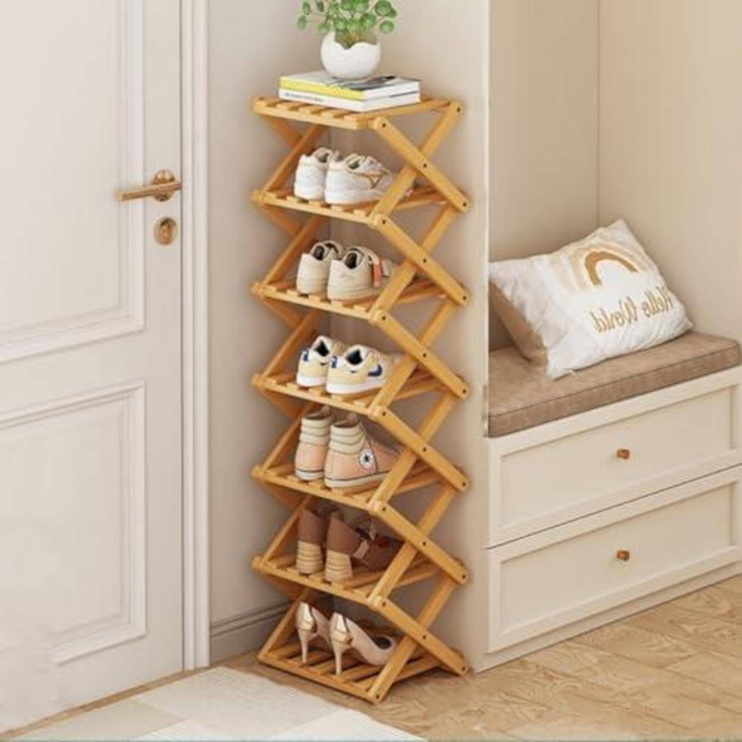Zusammenklappbares Holzschuhregal in einer Flurrecke mit mehreren Schuhpaaren und einer kleinen Pflanze oben neben einer eingebauten Bank.