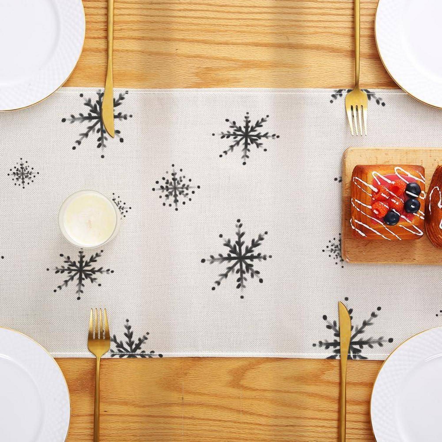 Draufsicht auf eine festliche Tischdecke mit weißen Tellern, goldenen Bestecken, einem Läufer mit Schneeflocken-Muster, einer Kerze und einem kleinen Dessertteller mit Beeren.