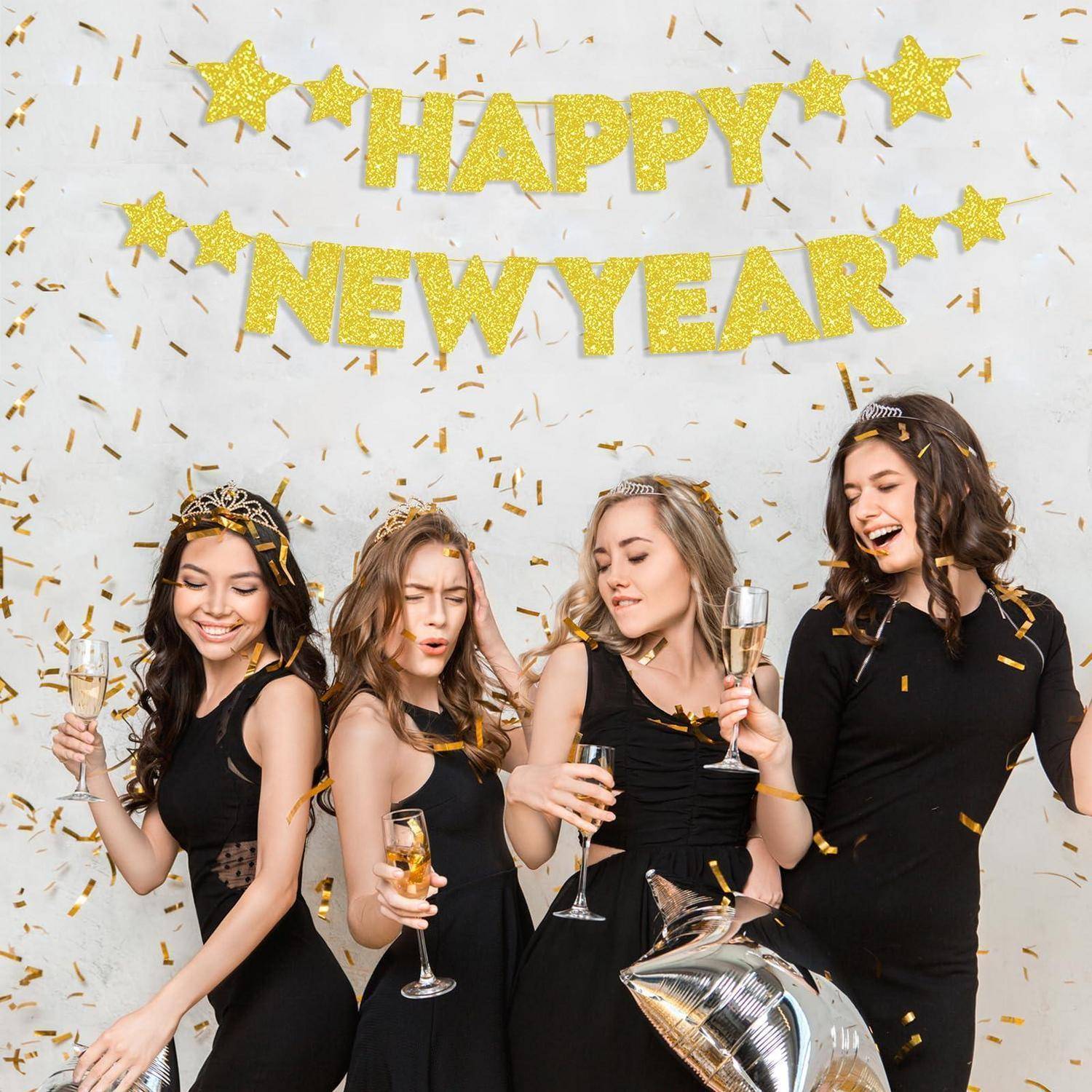 Vier Frauen in schwarzen Kleidern feiern Silvester mit Champagner und goldenem Konfetti unter einem Banner mit der Aufschrift „HAPPY NEW YEAR".