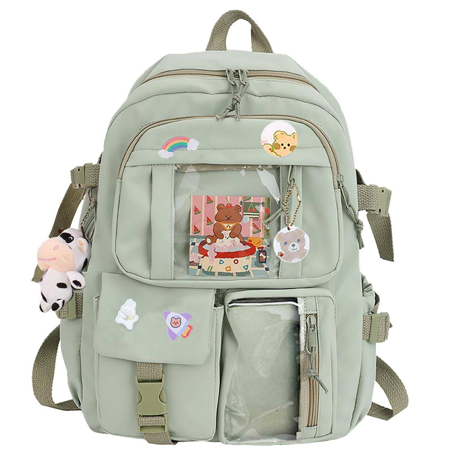 Mintgrüner Rucksack mit mehreren vorderen Taschen, transparentem Sichtfenster, Cartoon-Anstecknadeln und Plüsch-Schlüsselanhänger, der an der Seite hängt.