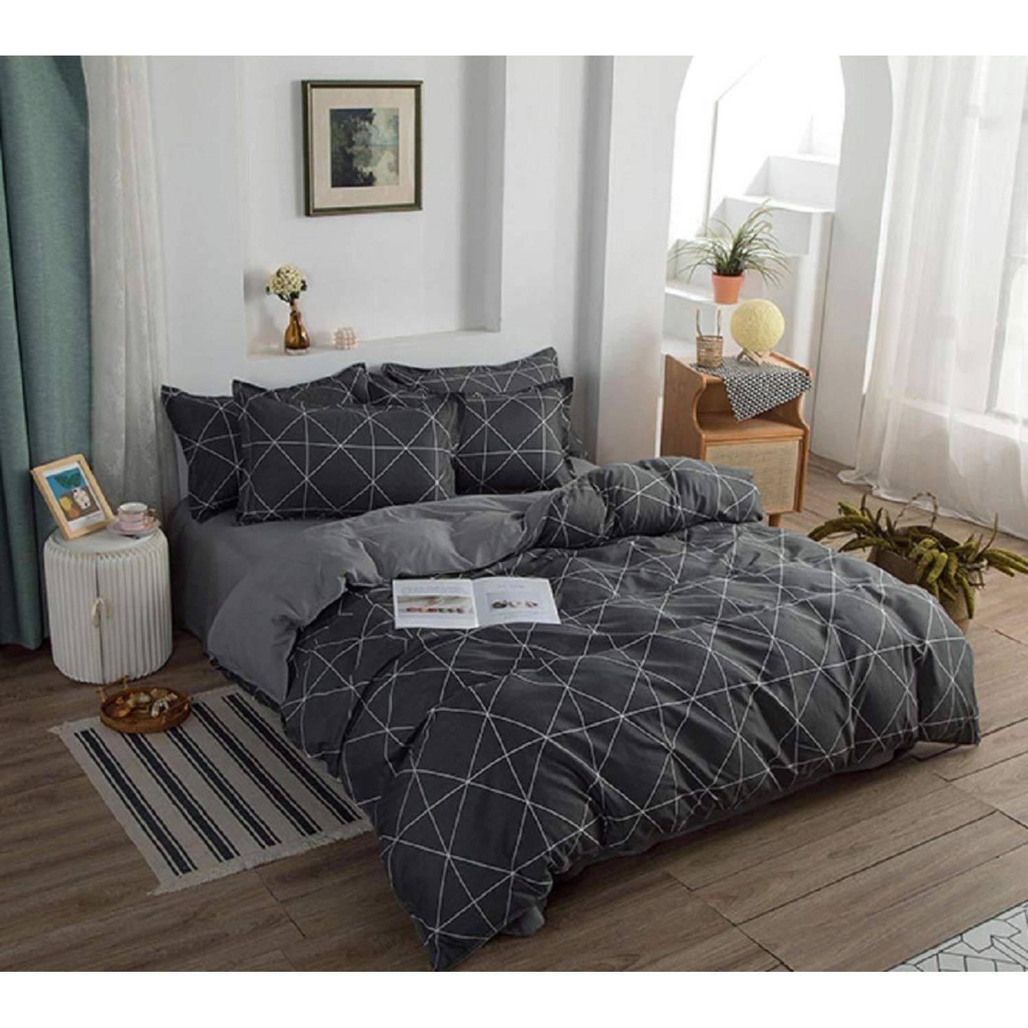 Ein ordentlich gemachtes Bett mit dunkler geometrischer Bettwäsche in einem hellen, minimalistischen Schlafzimmer mit einer Lampe, einer Pflanze, einem Nachttisch und gerahmter Wandkunst.