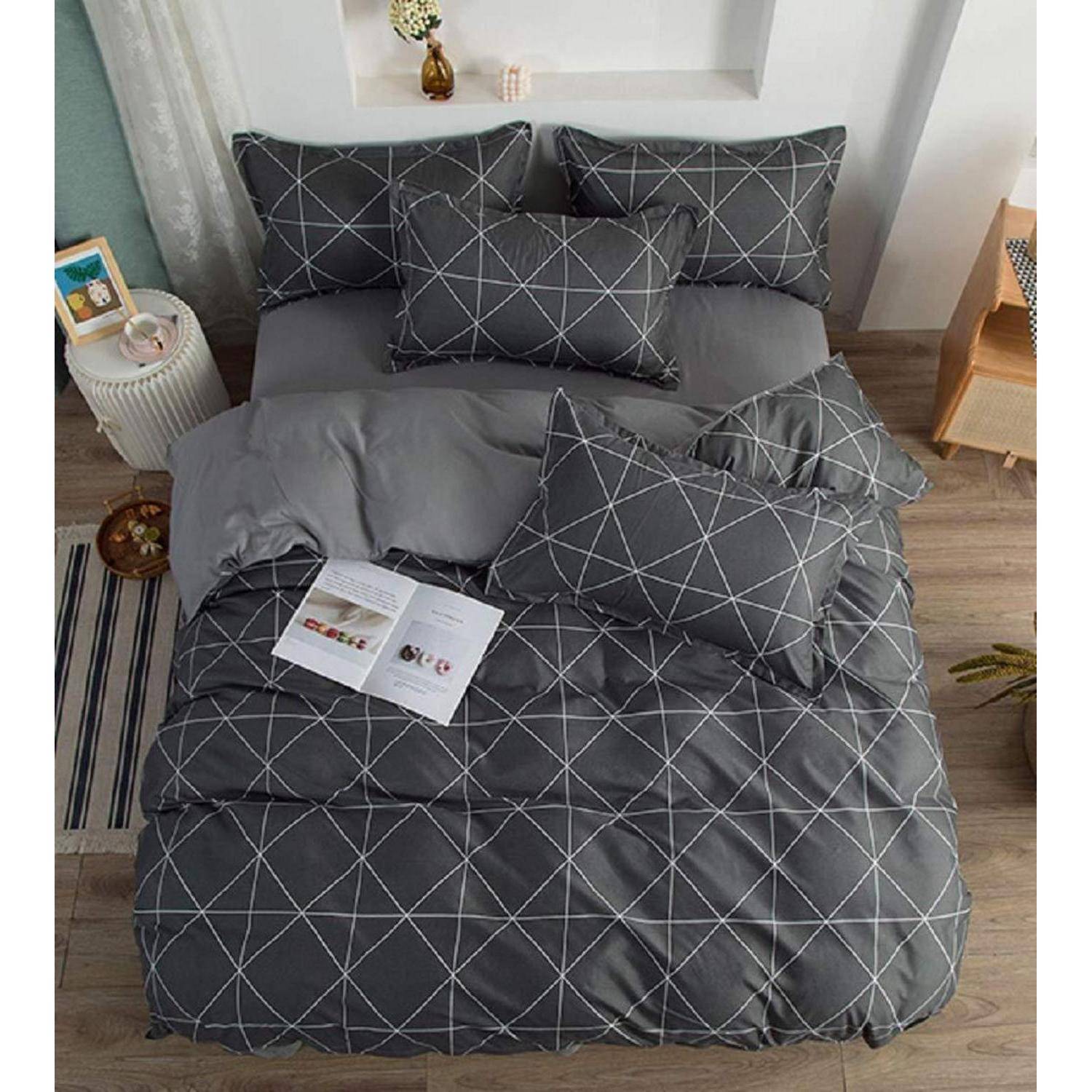 Draufsicht auf ein Bett mit dunkelgrauem geometrischem Bettzeug und mehreren Kissen, mit einem aufgeschlagenen Buch in der Nähe der Mitte.