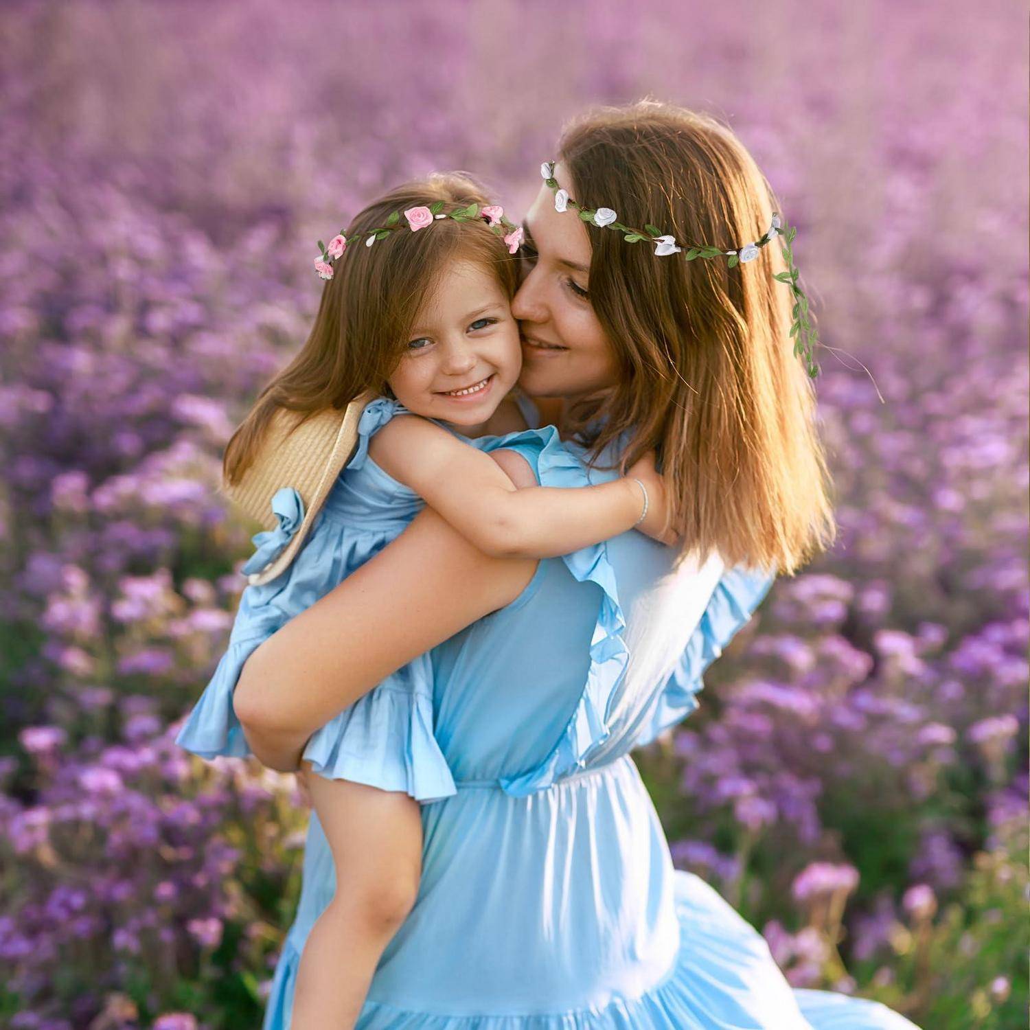Eine Frau in einem hellblauen Kleid umarmt ein lächelndes kleines Mädchen in einem Lavendelfeld, beide tragen Blumenkränze.