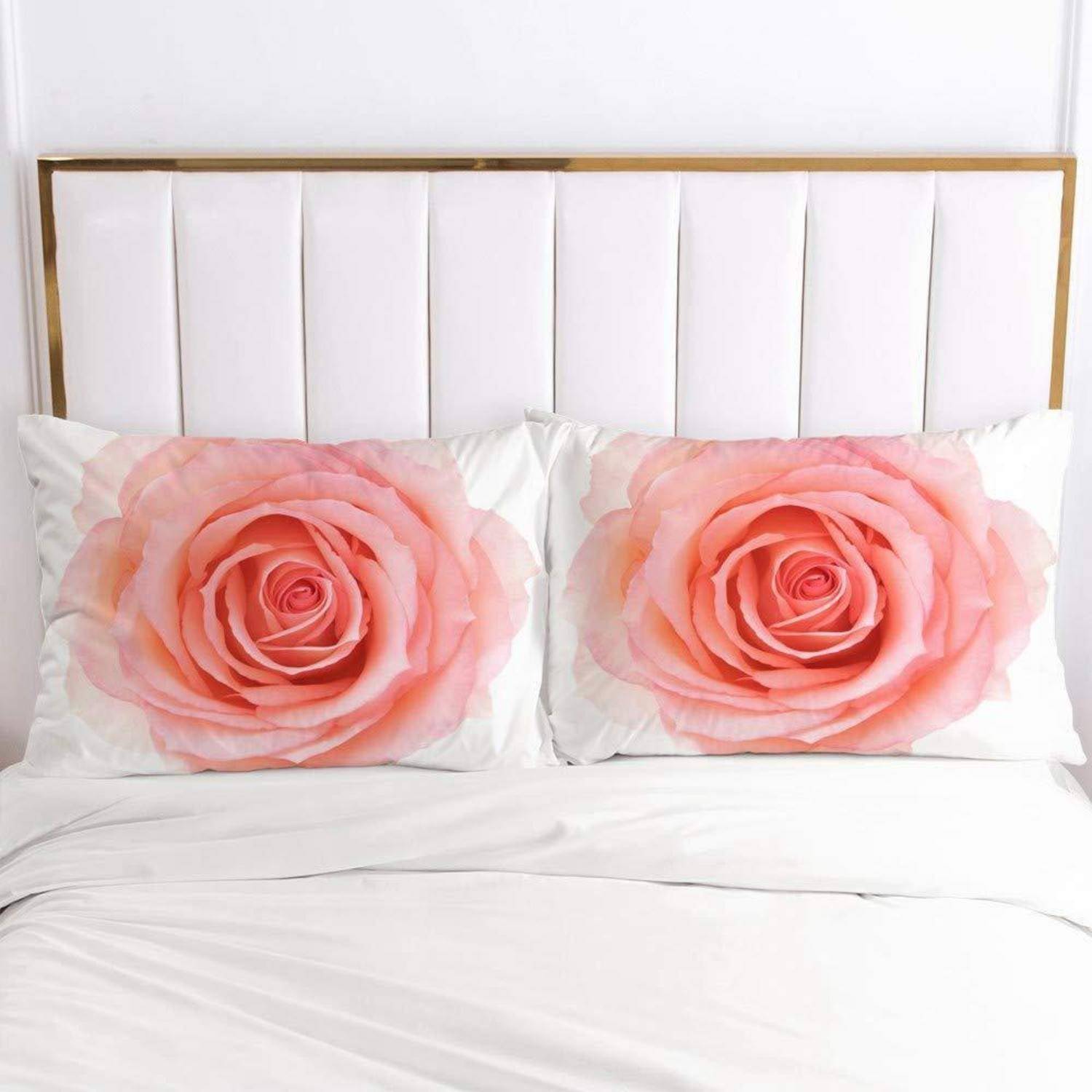 Ein ordentlich gemachtes weißes Bett mit zwei rosa bedruckten Rosenkissen vor einem weiß gepolsterten Kopfteil mit goldenem Rahmen.