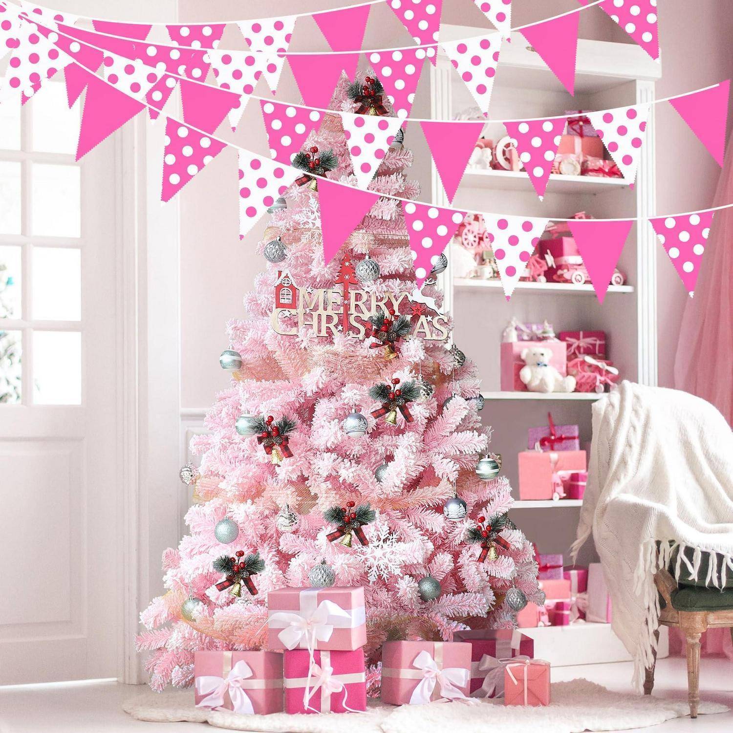 Rosa Weihnachtsbaum mit Ornamenten und Geschenkboxen in einem hellen Raum dekoriert, mit rosafarbenen Wimpeln und einem „Frohe Weihnachten"-Schild.