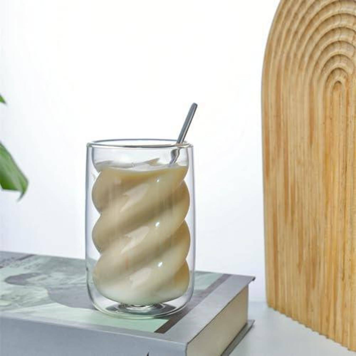 Glas mit gerührtem cremigem Getränk mit einem Löffel, das auf einem Buch neben einer Holzdekorplatte ruht.