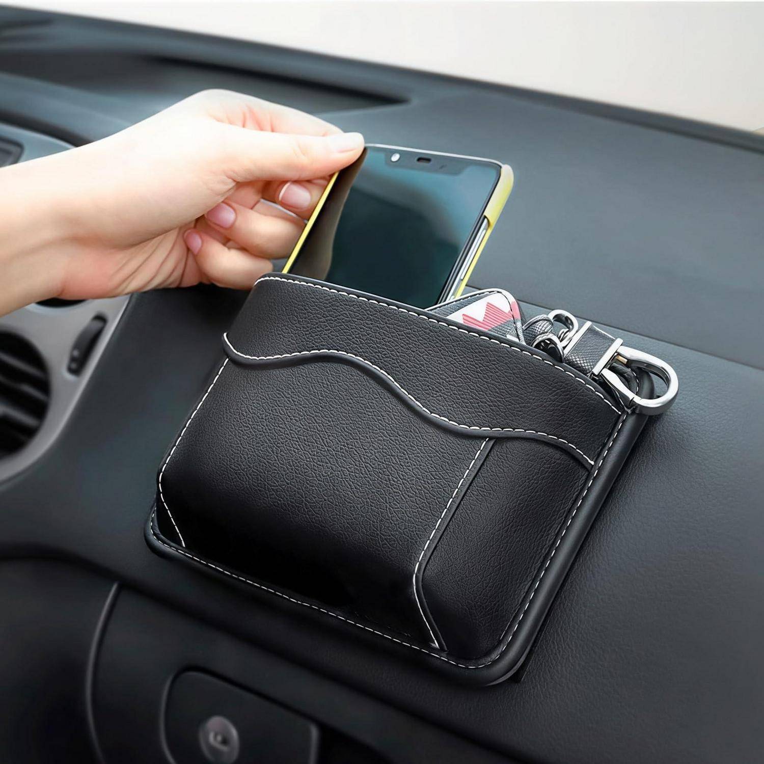 Hand, die ein Smartphone in eine schwarze Leder-Armaturenbrett-Aufbewahrungstasche legt, die an der Innenseite eines Autos befestigt ist.