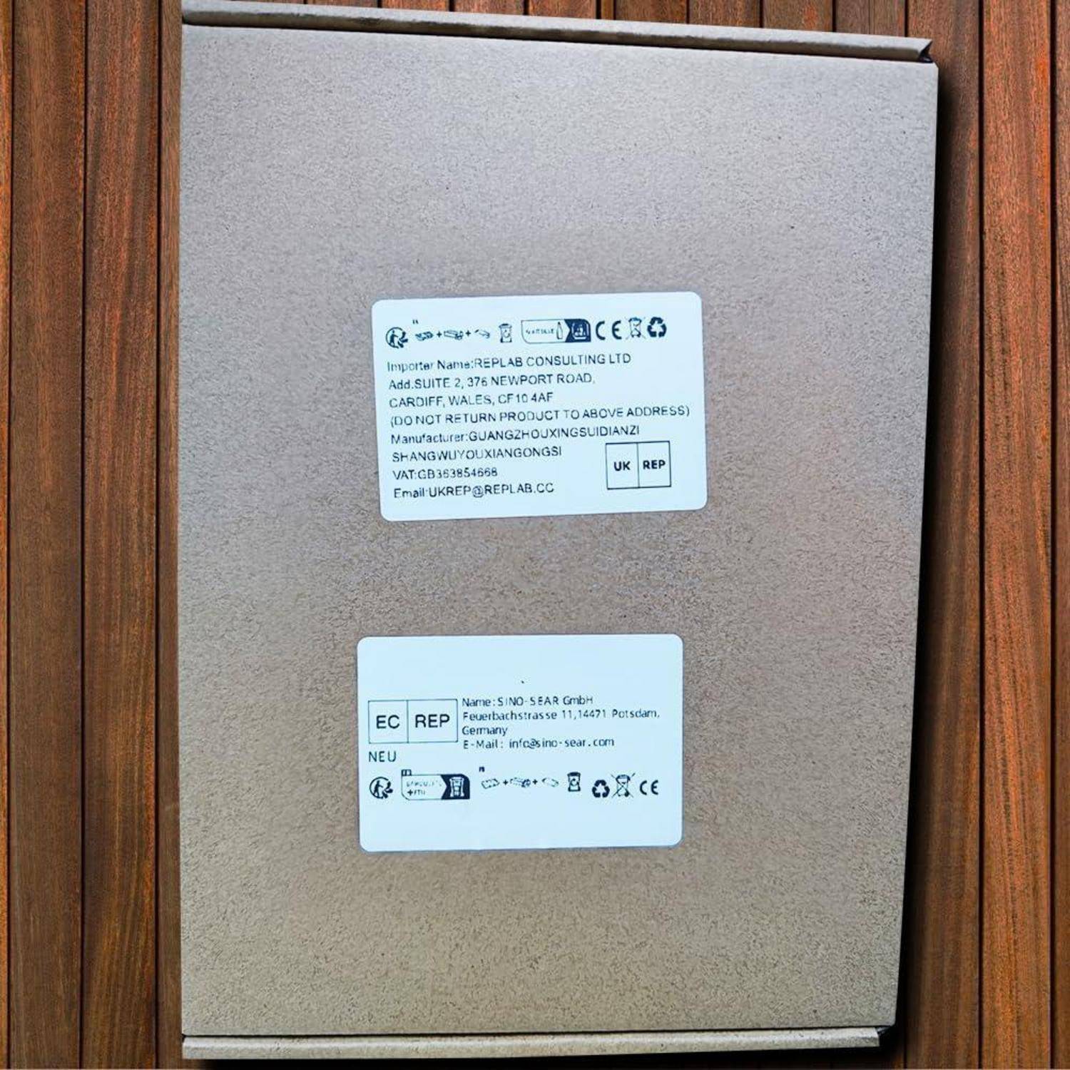 Karton-Versandbox mit zwei Regulierungsetiketten und Holzverkleidung im Hintergrund.