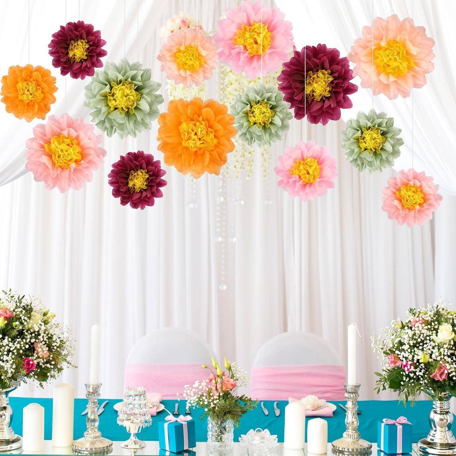 Pastellfarbener Blumen-Partyhintergrund mit hängenden Papierblumen über einem türkisfarbenen Desserttisch, weißen Stühlen, Kerzen, Geschenkboxen und Blumengestecken.