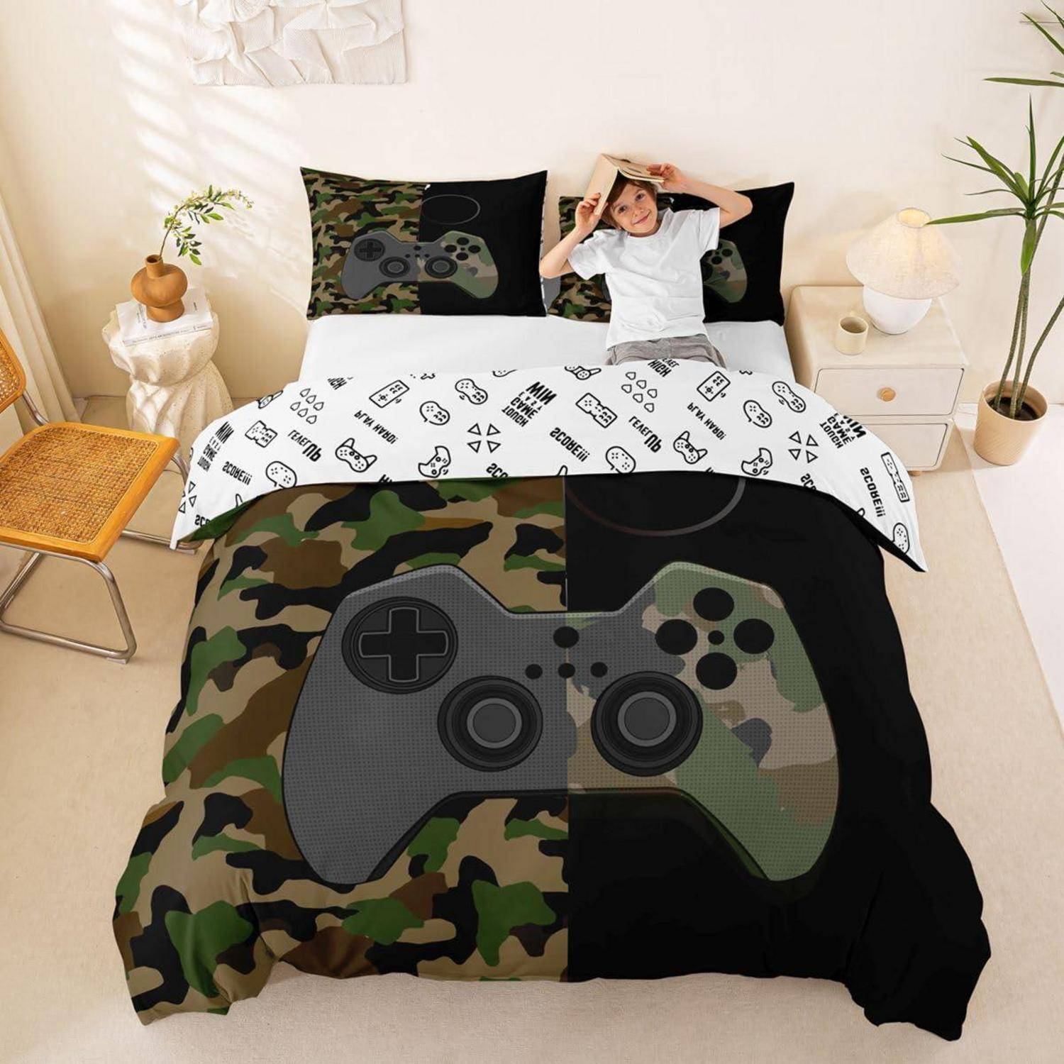 Junge, der auf einem Bett mit Spielcontroller-thematischer Bettwäsche liegt, einschließlich Tarn- und schwarzem Bettdecke und passenden Kissen in einem hellen Schlafzimmer.