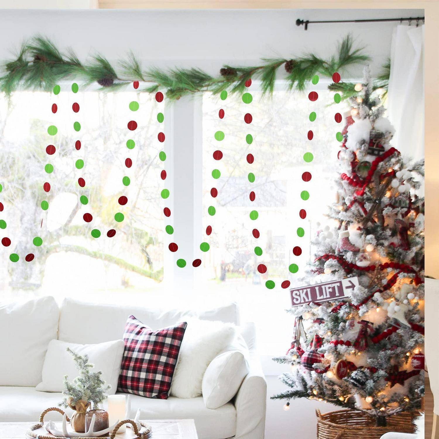 Festliches Wohnzimmer mit einem geschmückten Weihnachtsbaum neben einem weißen Sofa und weihnachtlicher Girlande, die das Wort „JOY" über dem Fenster buchstabiert.