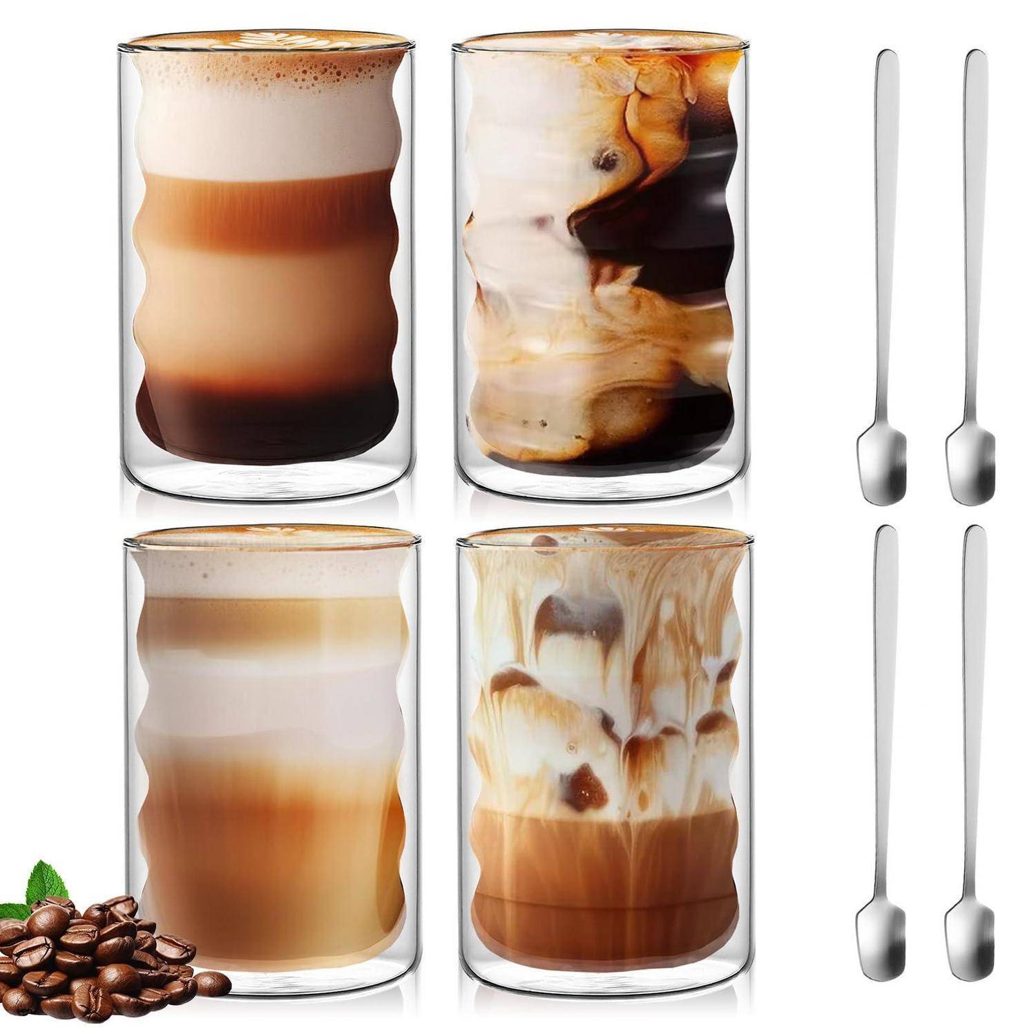 Vier doppelwandige Glaskaffeetassen mit geschichteten Getränken und Eis, dargestellt mit vier Edelstahlöffeln und Kaffeebohnen in der Ecke.