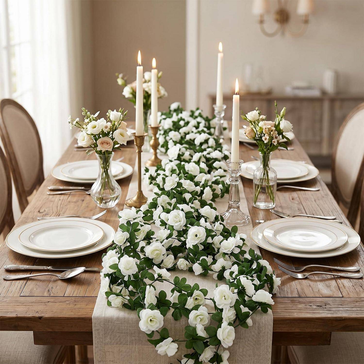 Eleganter Esstisch für ein formelles Event eingedeckt, mit weißen Tellern, Besteck, Kerzen und einer langen weißen Blumengestaltung in der Mitte.