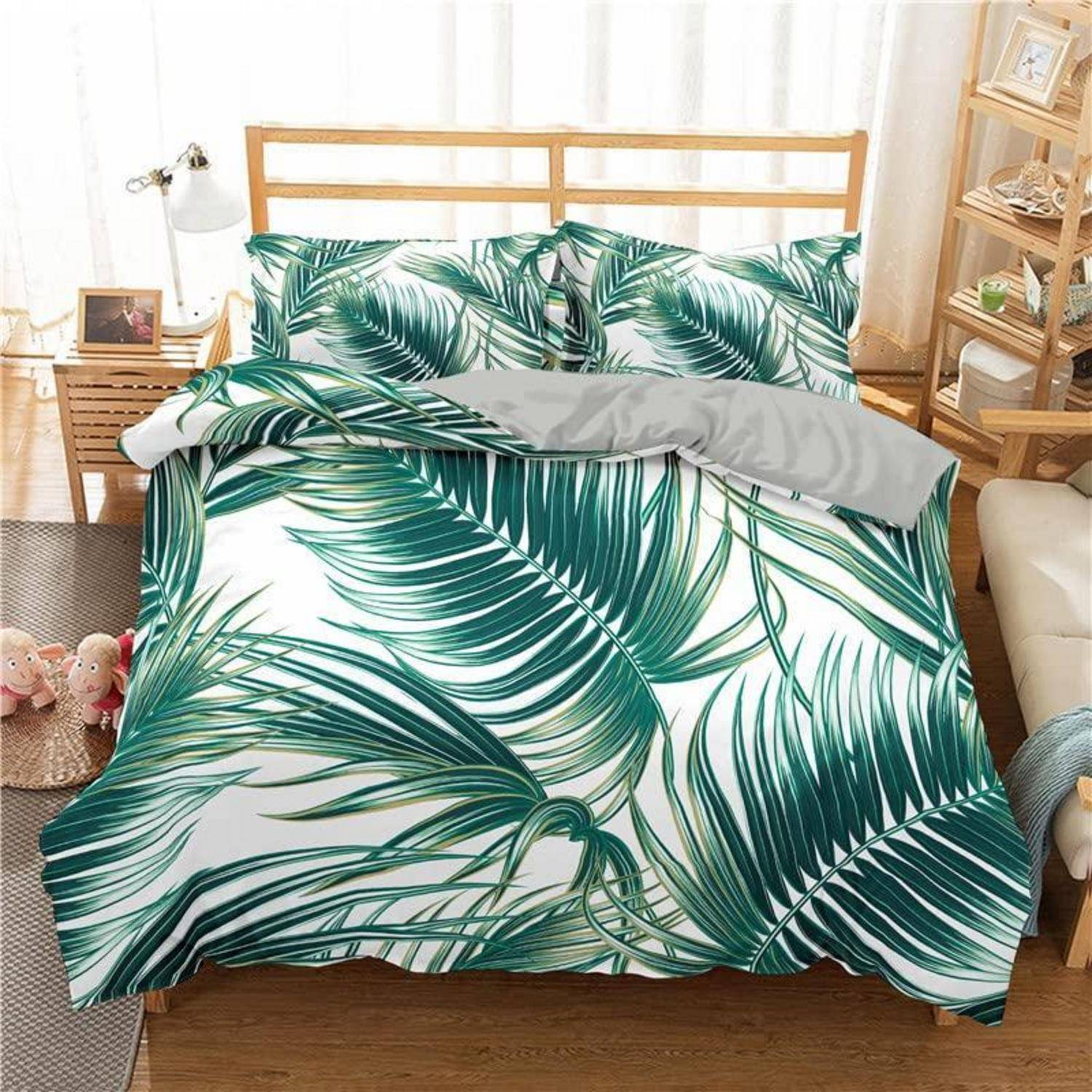 Ein ordentlich gemachtes Bett mit grüner tropischer Bettbezug-Kollektion und passenden Kissen in einem hellen Schlafzimmer, mit einer grauen Wurfdecke, die über die Oberseite drapiert ist.