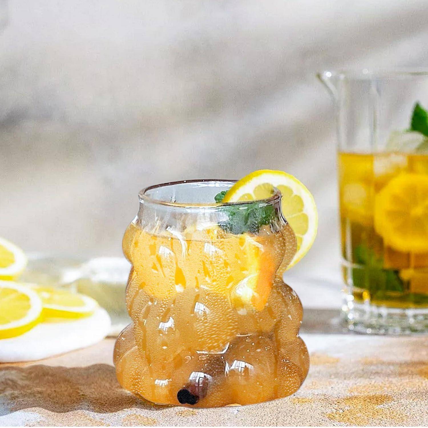 Ein Glas mit eiskaltem Zitrusgetränk, garniert mit Zitrone und Minze, mit einem zweiten Zitronengetränk im Hintergrund.