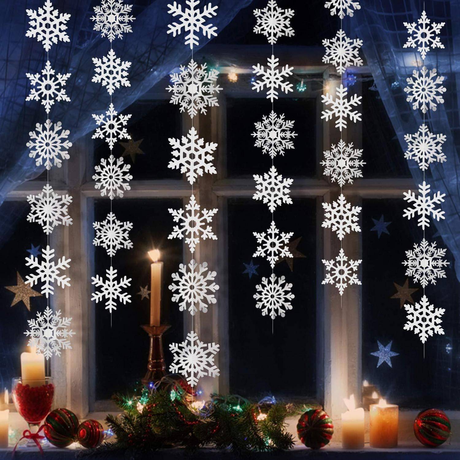 Fenster, das zu Weihnachten mit hängenden Schneeflocken, brennenden Kerzen, Christbaumkugeln und Grünzeug auf der Fensterbank in der Nacht dekoriert ist.