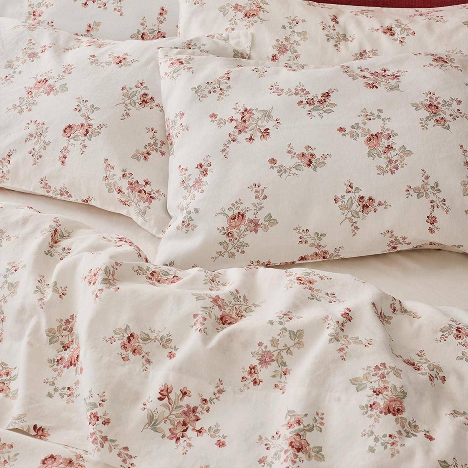 Nahaufnahme eines Bettes mit weiß gemusterter Bettwäsche mit Blumenmotiven und Kissen in sanften Rosa- und Grüntönen.