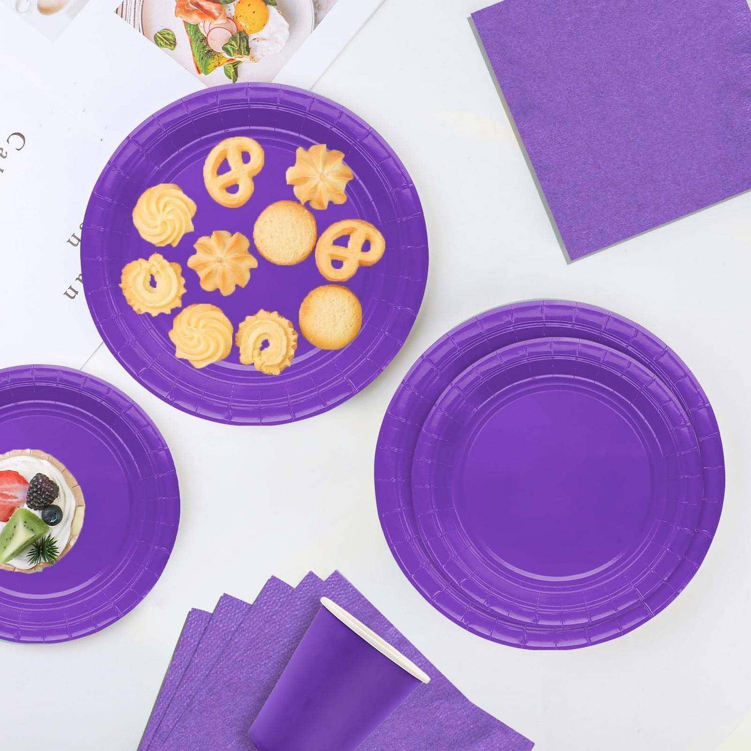 Lila Partygeschirr-Set mit Papierservierplatten, Bechern, Servietten und einem Nachtischteller mit gemischten Keksen und fruchtgedeckten Leckereien.