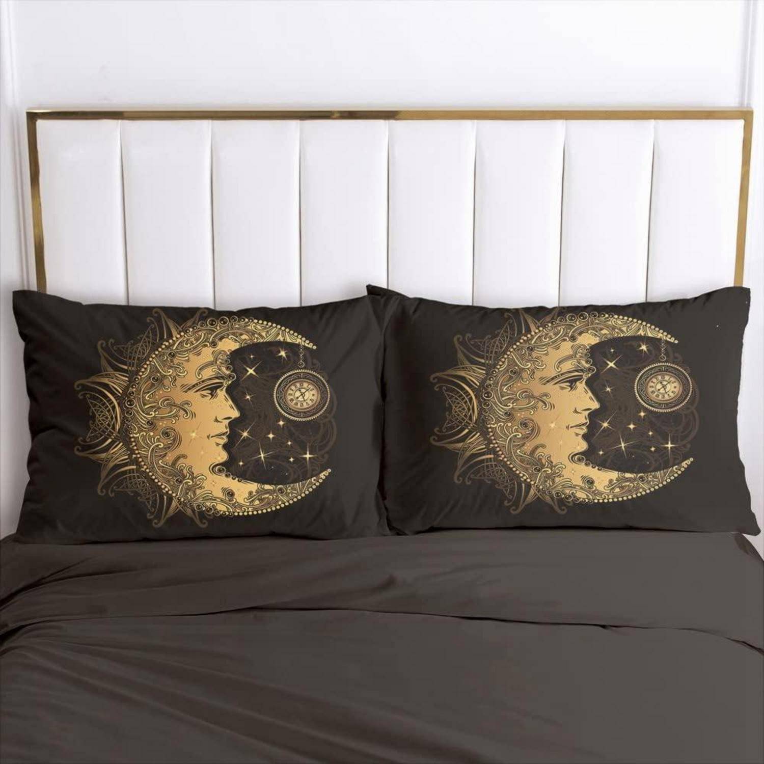 Bett mit zwei schwarzen Kissen mit passenden gold-farbenen Mond- und Gesichtsdesigns vor einem weiß gepolsterten Kopfteil.