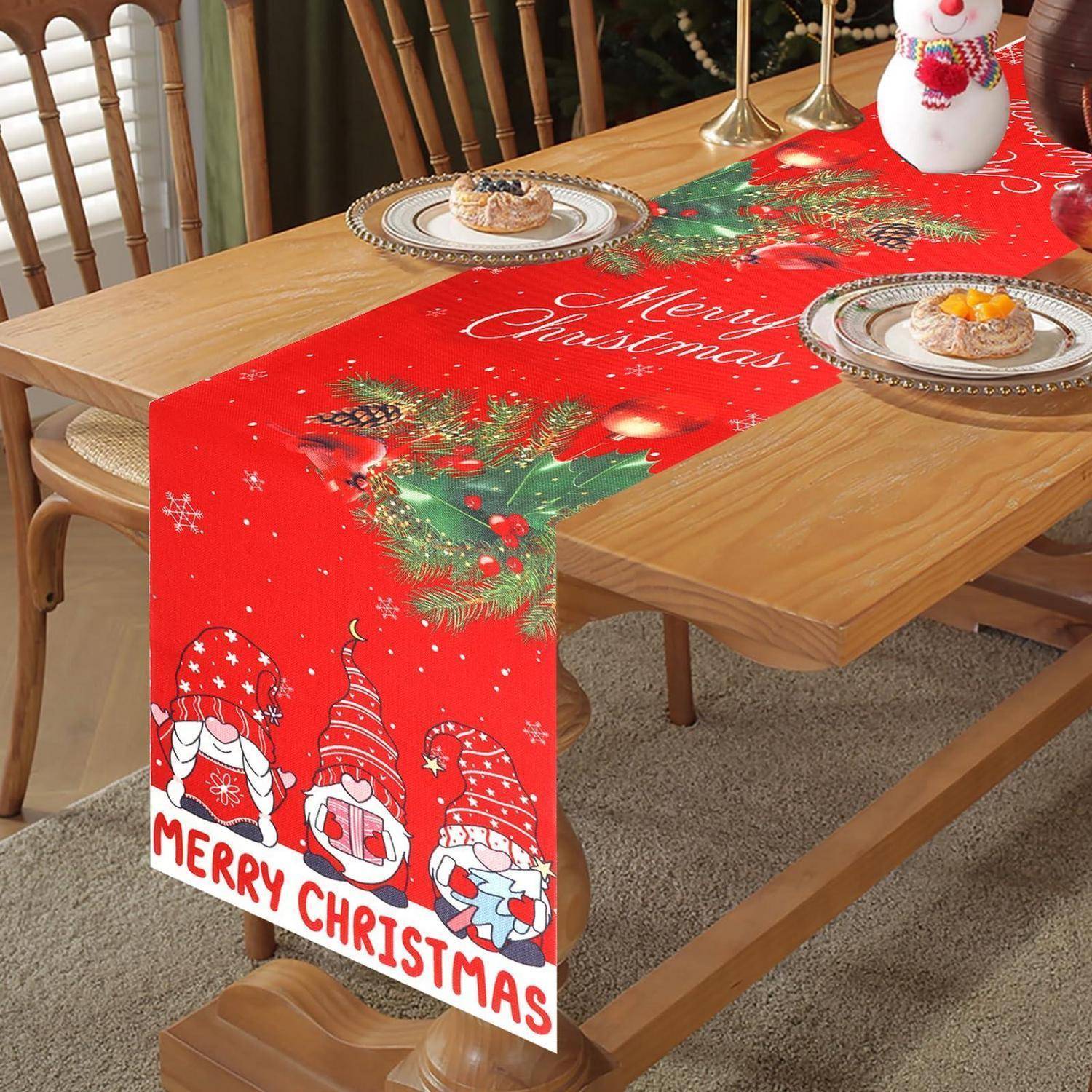 Tischläufer zu Weihnachten auf einem Esstisch mit 'Frohe Weihnachten'-Text, Weihnachtszwergen und festlichen Tellern und Dekoration.