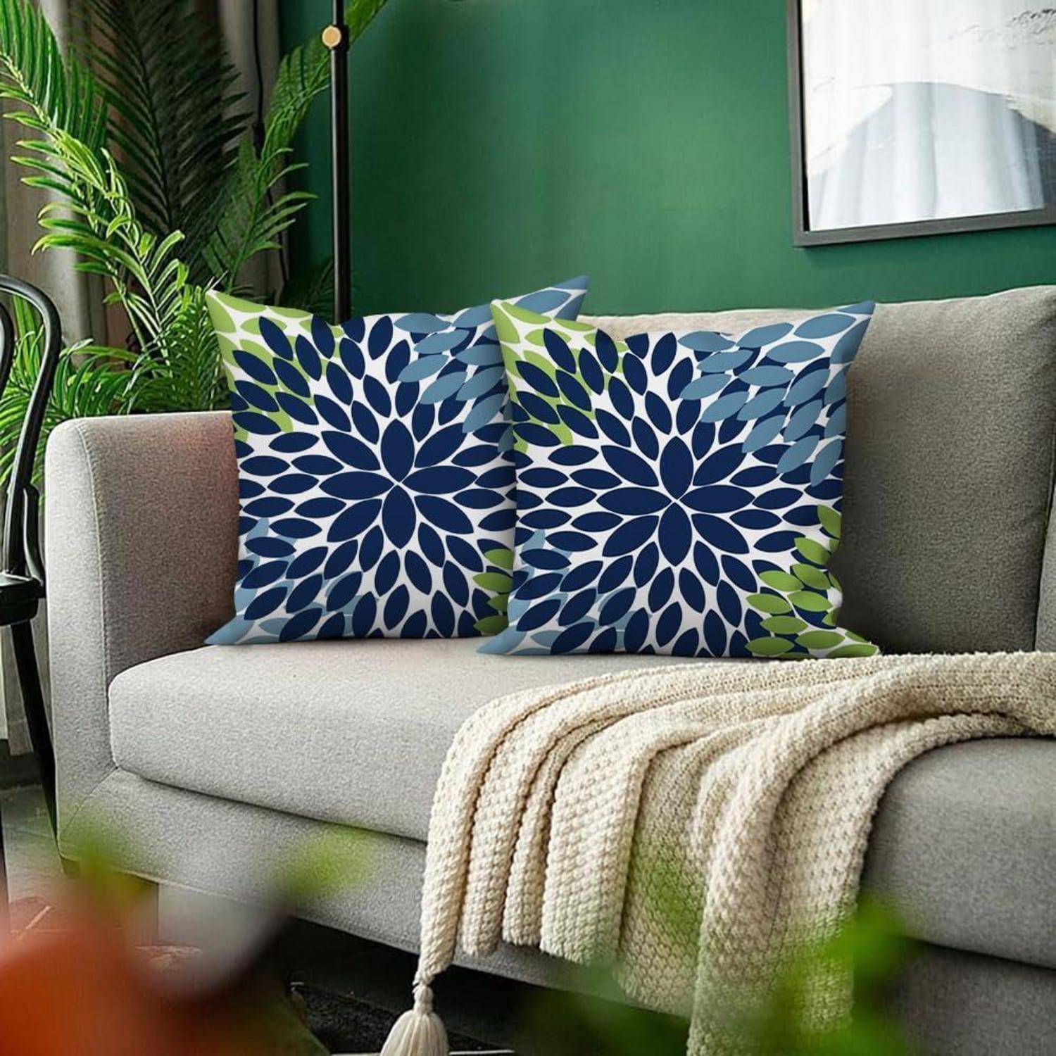 Modernes graues Sofa mit zwei blau-grün gemusterten Kissen und einer cremefarbenen Strickdecke in einem grünen Wohnzimmer.