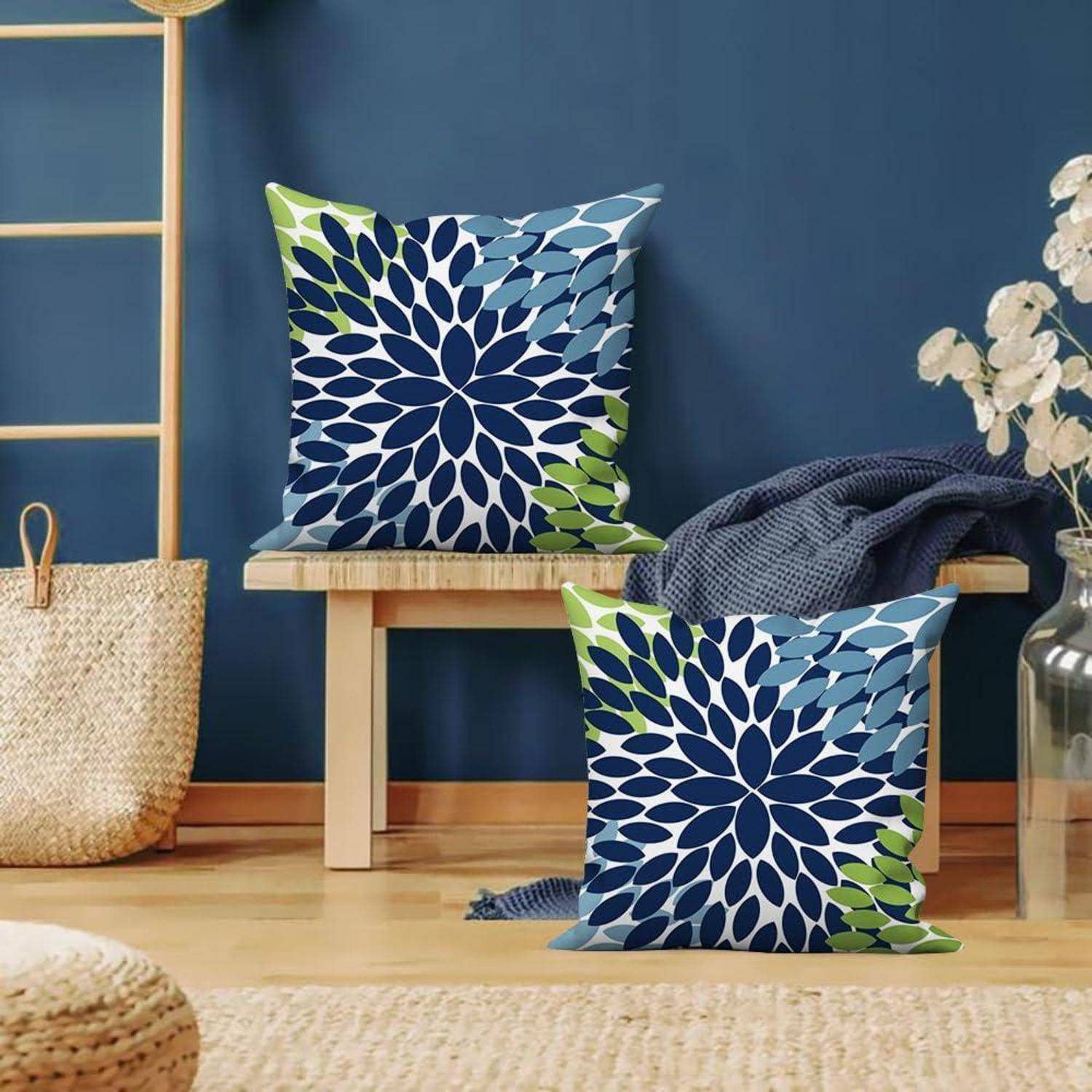 Zwei dekorative quadratische Kissen mit blau- und grüngemusterten Bezügen mit Blattmotiven auf einer Holzbank in einem gemütlichen Zimmer.