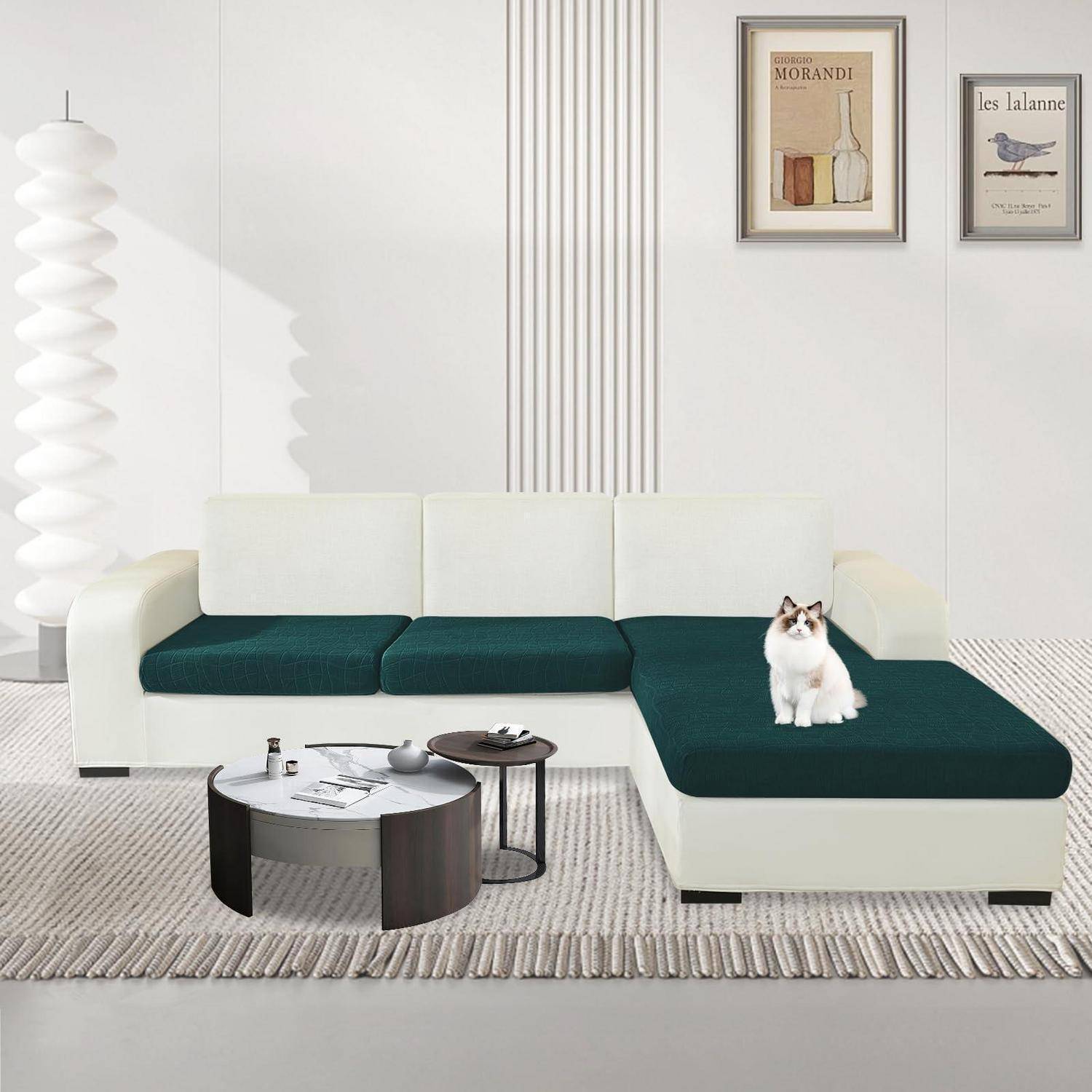 Modernes Wohnzimmer mit weißem Ecksofa, dunkelgrünen Kissen, Couchtischen, Stehlampe, gerahmter Kunst und einer Katze, die auf der Récamière sitzt.