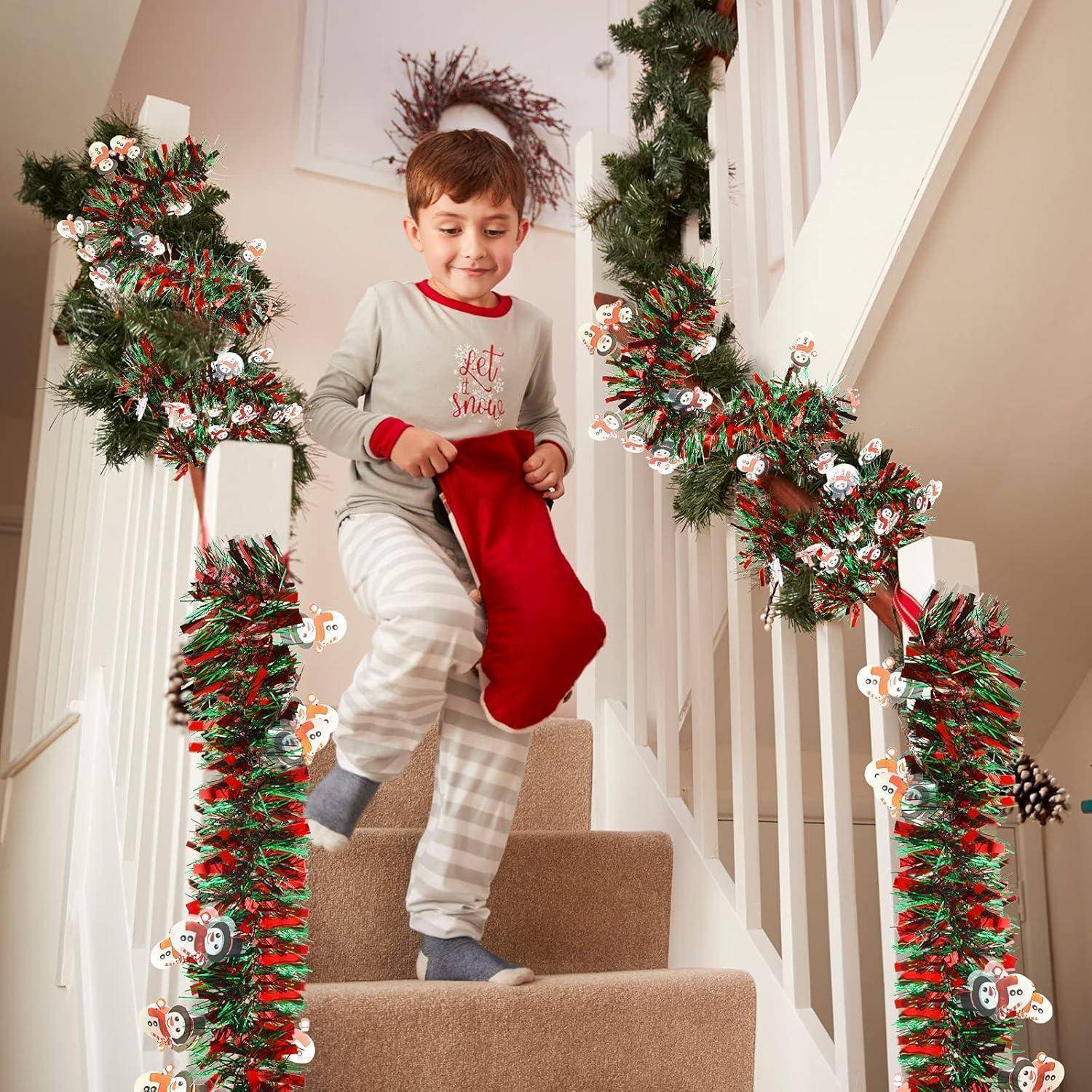 Kind in Schlafanzug steigt eine geschmückte Treppe hinunter und hält am Weihnachtsmorgen einen roten Weihnachtsstrumpf in der Hand.