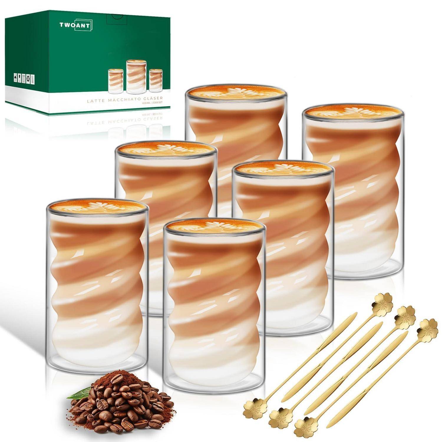 Sechs Latte-Macchiato-Gläser mit geschichteten Kaffeegetränken, eine Produktschachtel im Hintergrund, Kaffeebohnen und Rührstäbchen auf einer weißen Oberfläche.