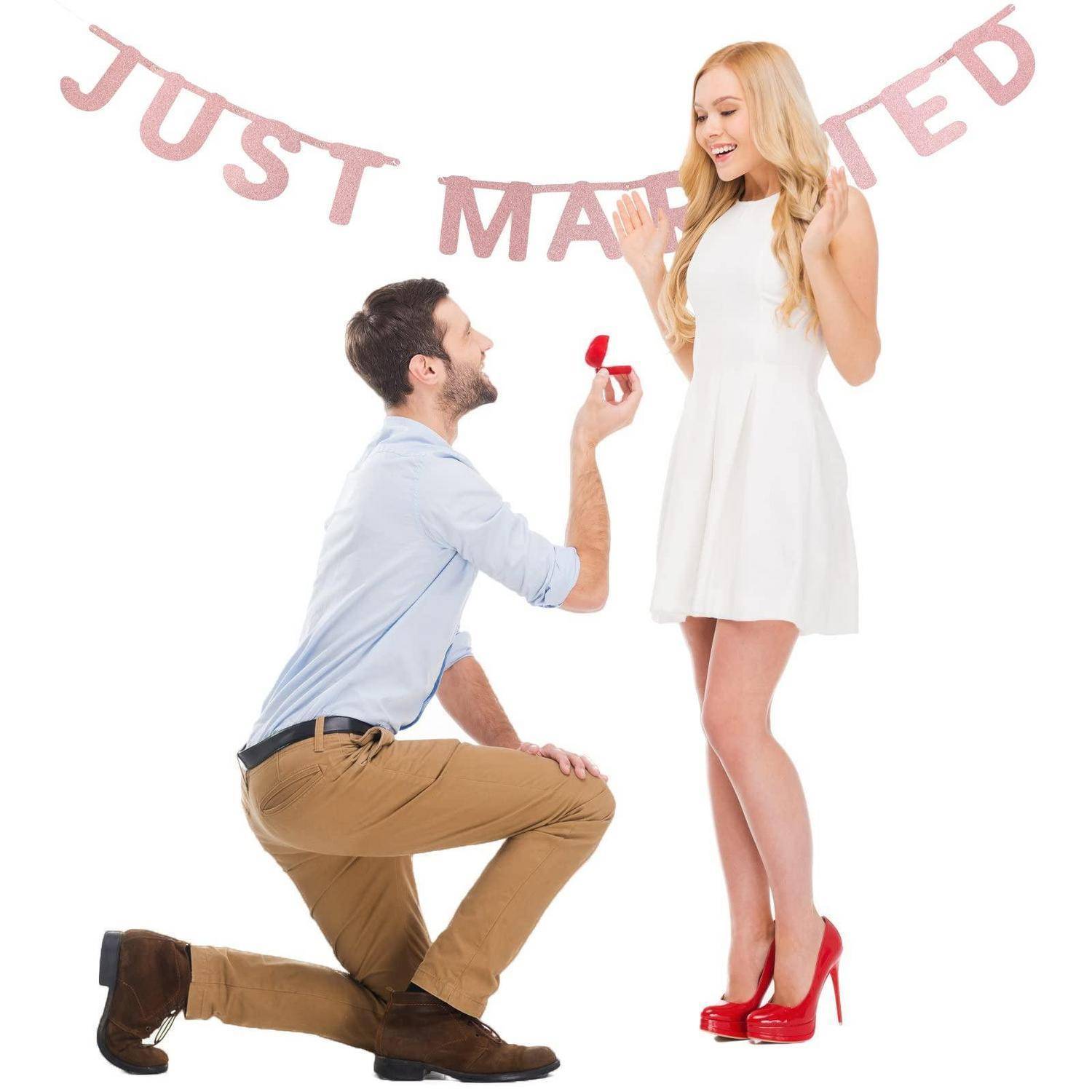 Ein Mann macht einer lächelnden Frau einen Heiratsantrag mit einem Ring unter einem "Gerade verheiratet""-Banner.