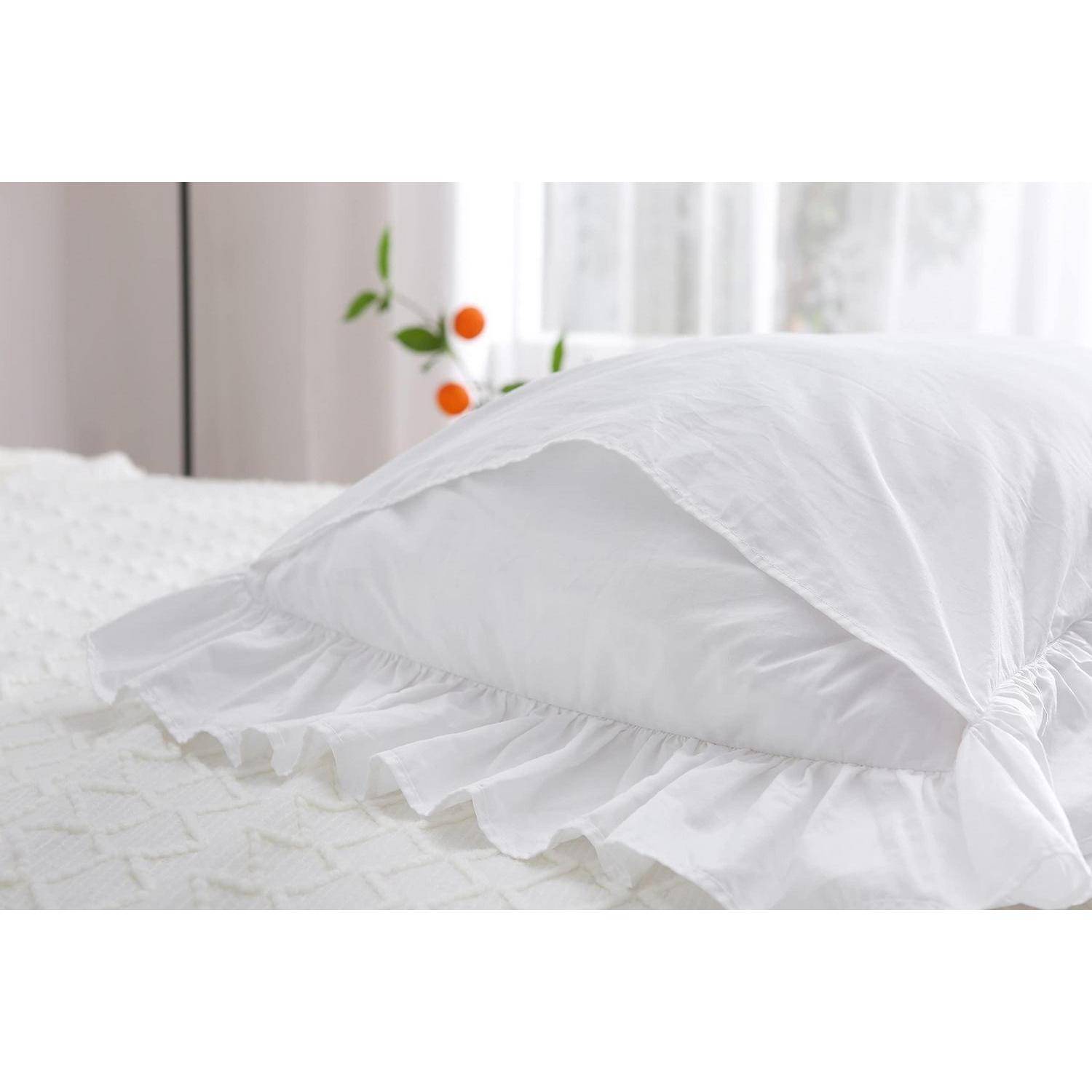 Weißes Kissen mit gerüschter Kante, das auf einem weißen Bett in einem hellen Schlafzimmer ruht.