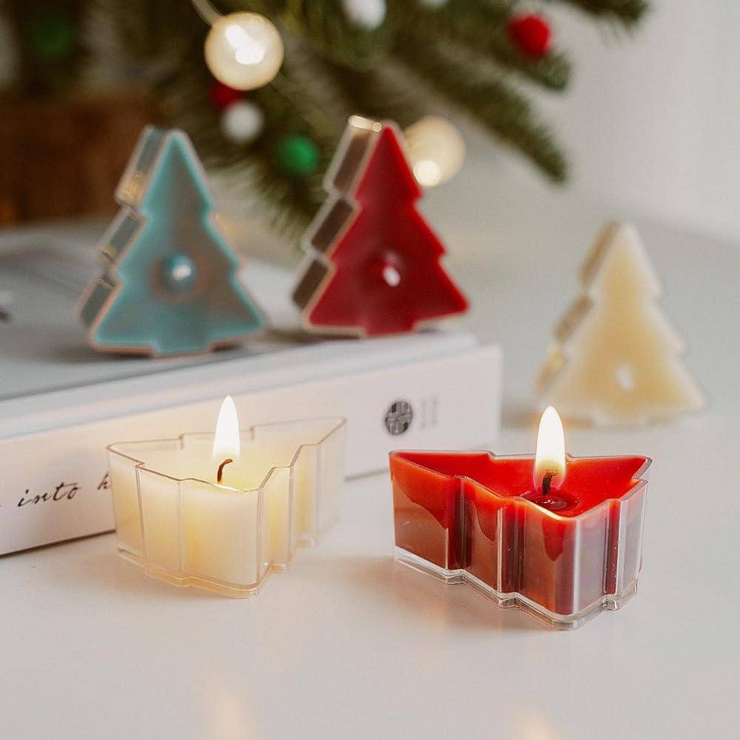 Zwei brennende dekorative Kerzen in klaren weihnachtsbaumförmigen Haltern, mit drei kleinen Baumkugeln im Hintergrund.