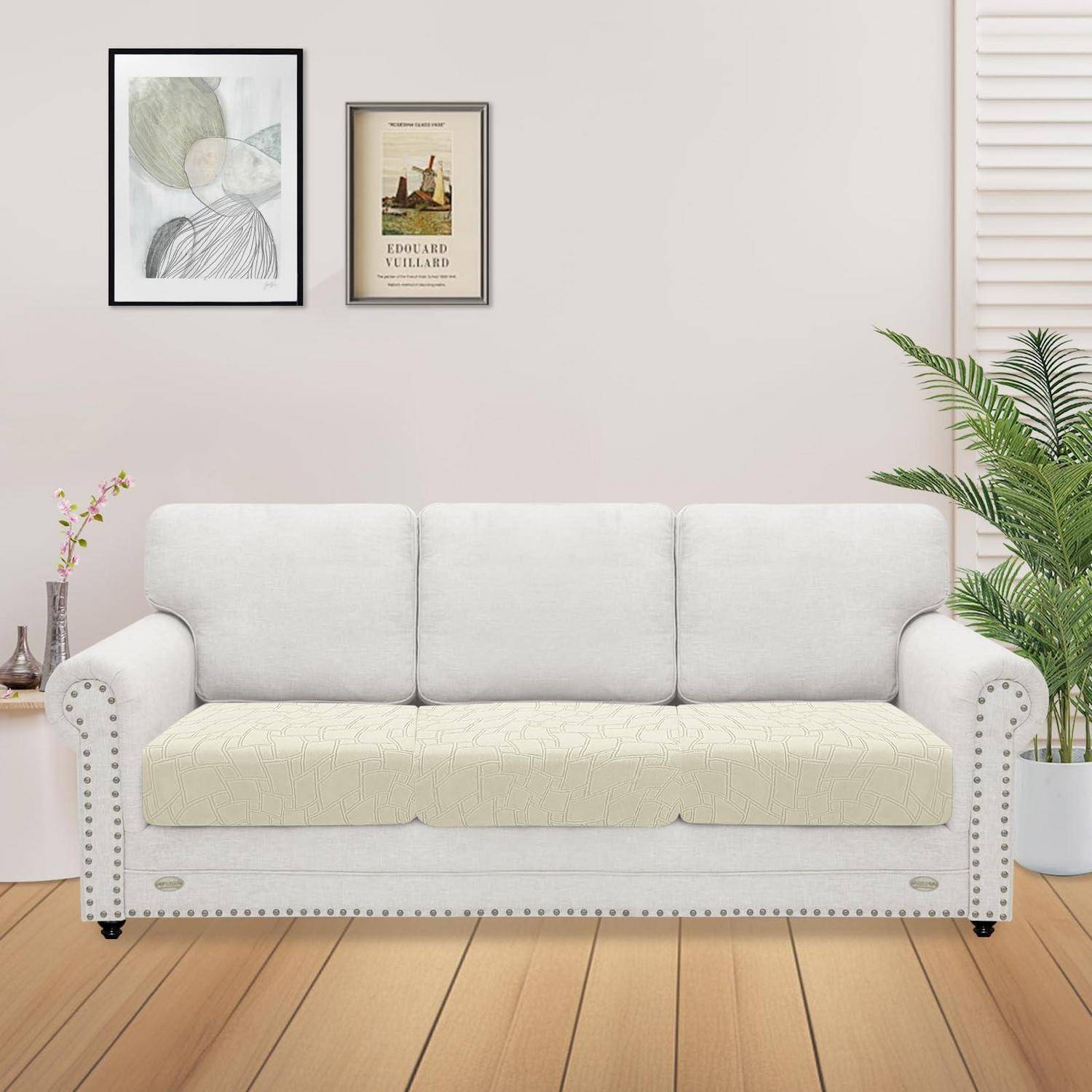 Weiches Dreisitzer-Sofa mit hellem Kissen und genieteten Armlehnen in einem hellen Wohnzimmer, mit gerahmten Wandbildern und Topfpflanzen.