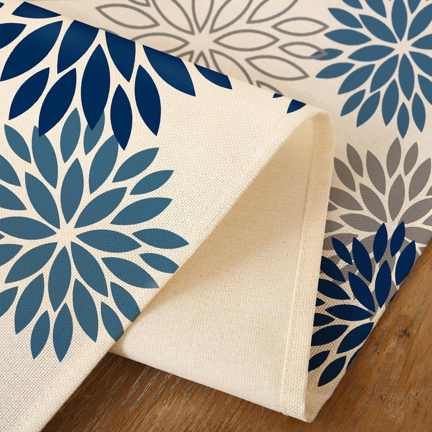 Gemusterte Stoffmuster mit blauen floralen Blattkmustern auf beigefarbenem Canvas, gefaltet, um Textur und Farboptionen zu zeigen.