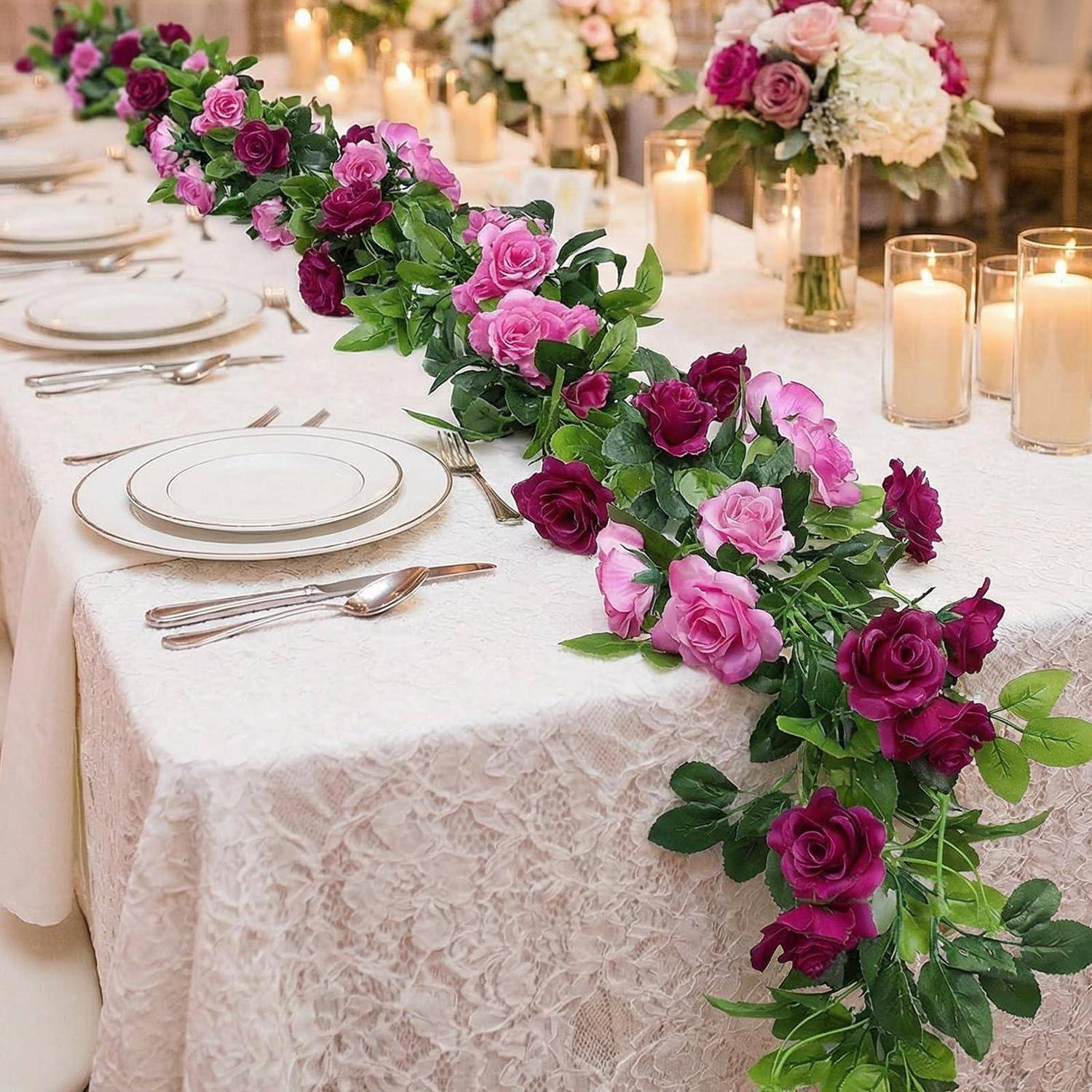 Eleganter Festtisch mit weißer Spitzentischdecke, goldfarbig geränderten Tellern, Kerzen und einer kaskadierfförmig angeordneten Tafelaufsatz aus rosa und violetten Rosen.
