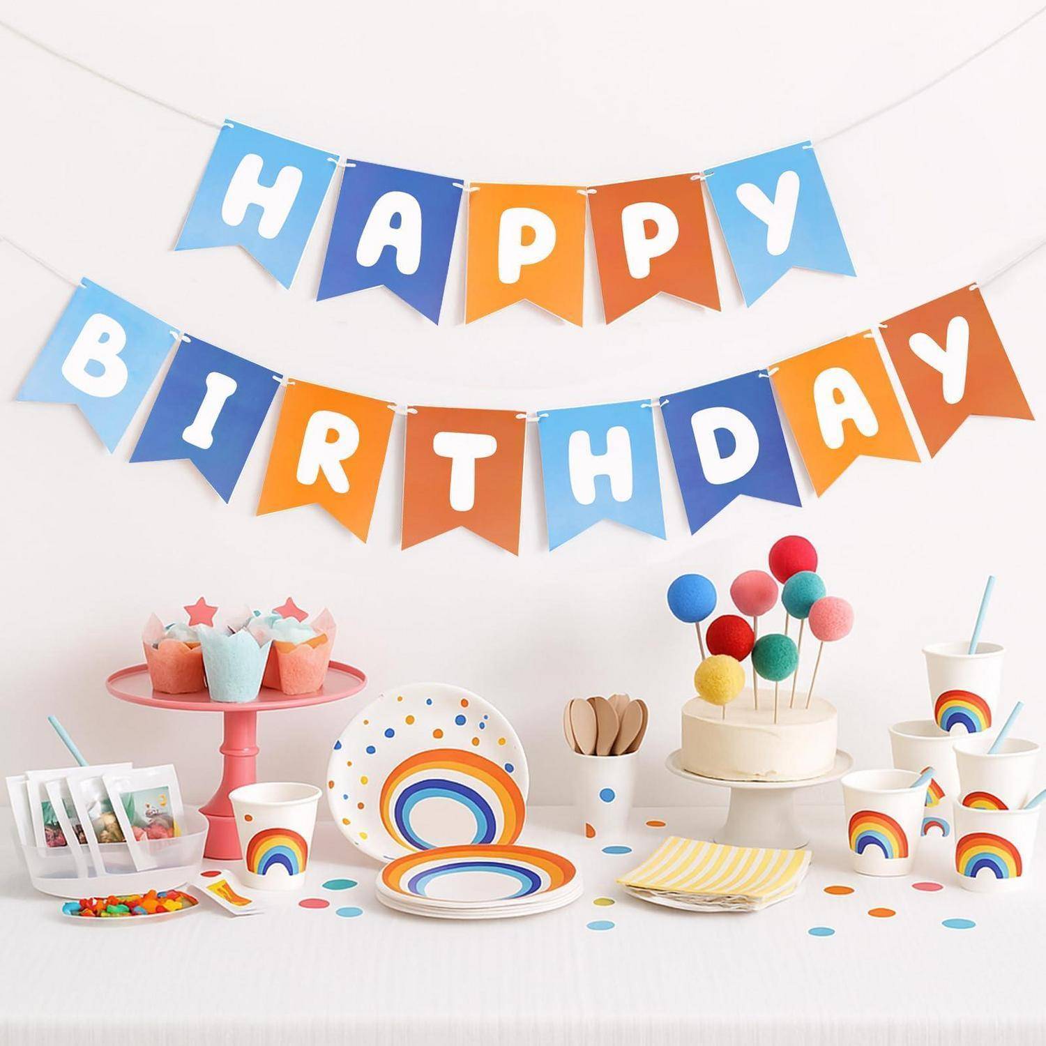 Geburtstagsfeier-Tischdekoration mit bunten "ALLES GUTE ZUM GEBURTSTAG""-Bannern, regenbogenfarbigen Tellern und Bechern, Cupcakes, Kuchen mit Luftballons und Partygeschenken.