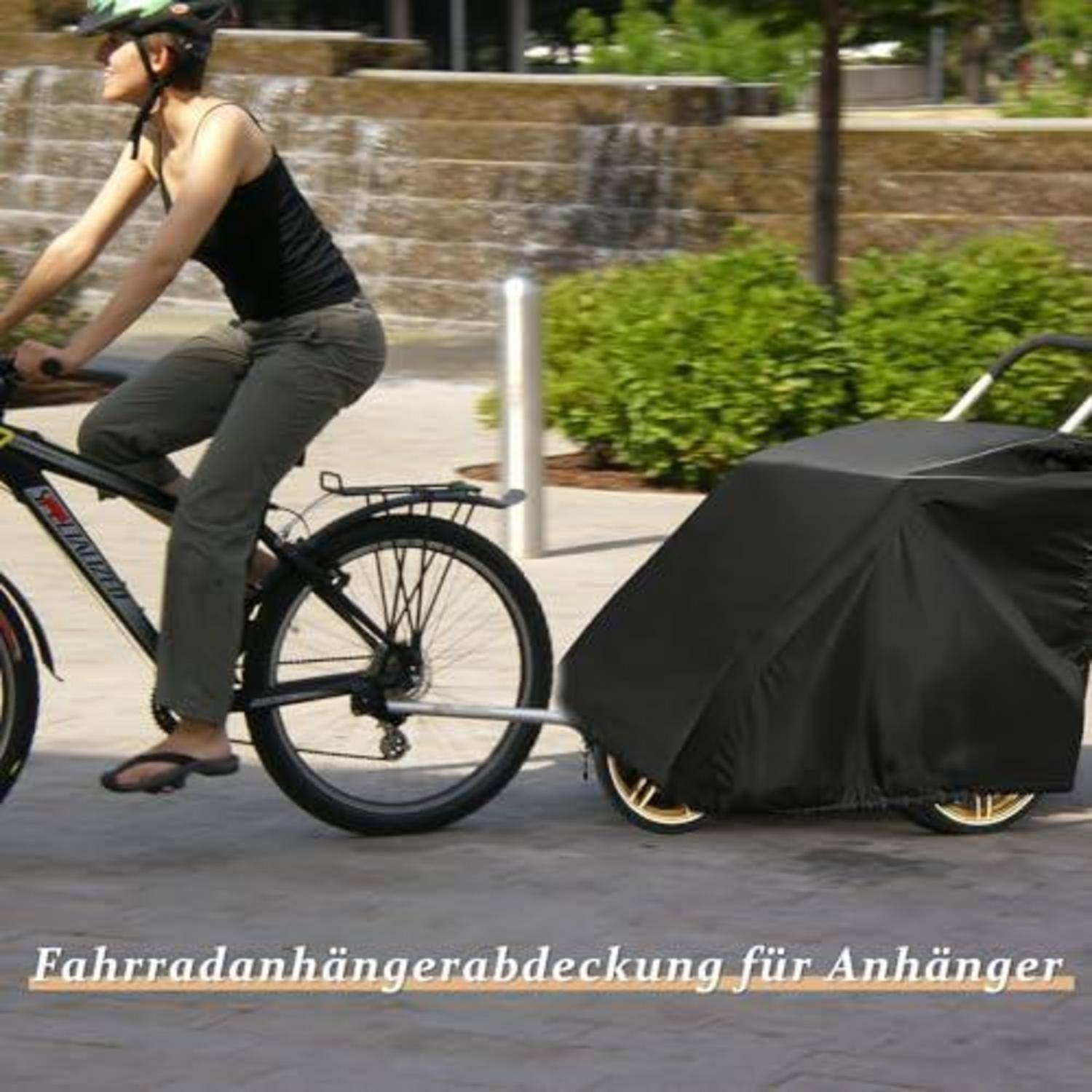 Frau auf einem Fahrrad, die einen abgedeckten Anhänger zieht; der Anhänger ist unter einer schwarzen Schutzplane verborgen.