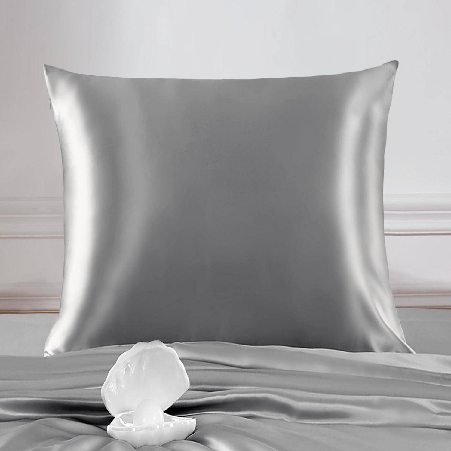 Silberner Satinkissenbezug auf einem Bett mit einem weißen muschelförmigen Dekorationsobjekt davor, vor einer hellgrauen Wand.