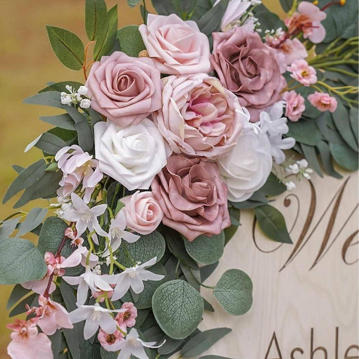 Zartes Bouquet aus rosa, weißen und mauvefarbenen Rosen mit Grünwerk und Orchideen, die um den Namen „Ashley" auf einem Schild herum arrangiert sind.