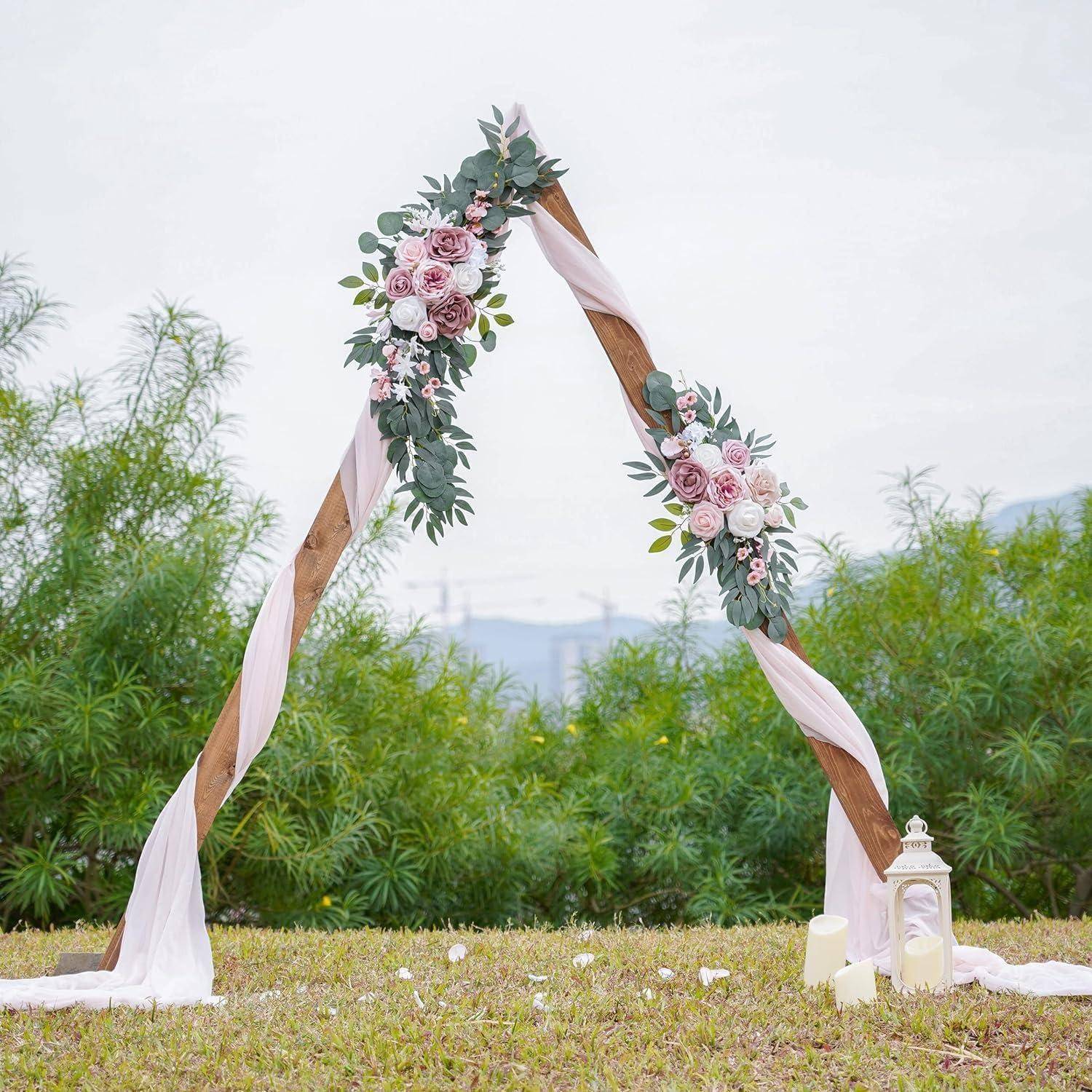 Blumenbogen für Hochzeit im Freien, dekoriert mit rosa Rosen, Grünwerk und weißer Drapierung, mit Laternen und Kerzen an der Basis.