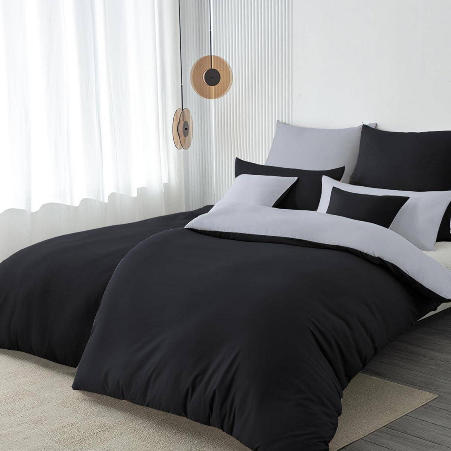 Modernes Schlafzimmer mit einem Bett aus schwarzer, grauer und weißer Bettwäsche neben einem hellen Fenster und hängender Wanddekoration.