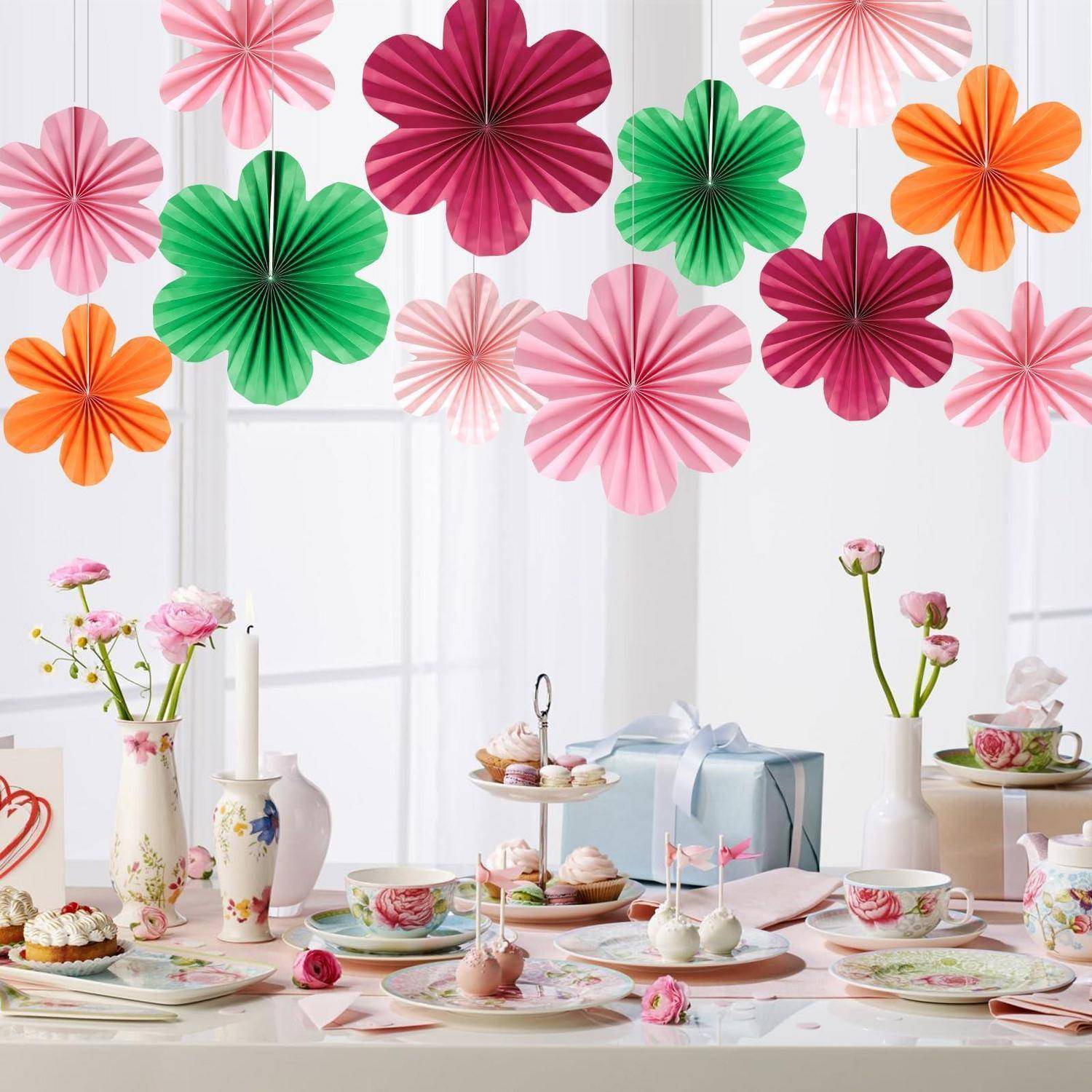 Pastell-Partytisch mit Teetassen, Desserts, Blumen und einer Geschenkbox unter bunten Papierblutendekorationen.