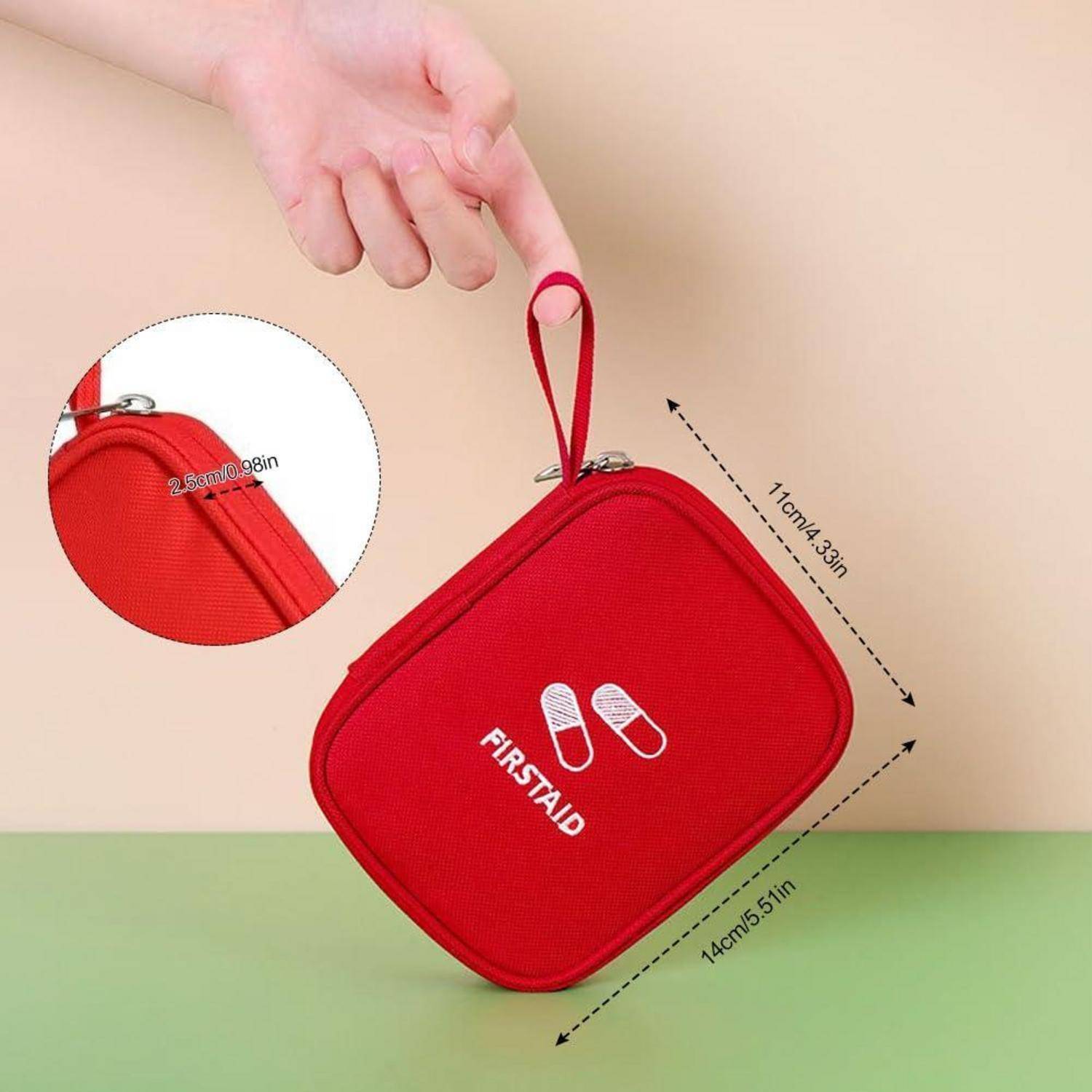Hand hält eine rote Erste-Hilfe-Tasche mit Reißverschluss, Schlaufengriff und weißem „FIRSTAID"-Symbol; Ausschnitt zeigt Nahaufnahme der Nähte mit Größenangaben von 14 cm x 11 cm.