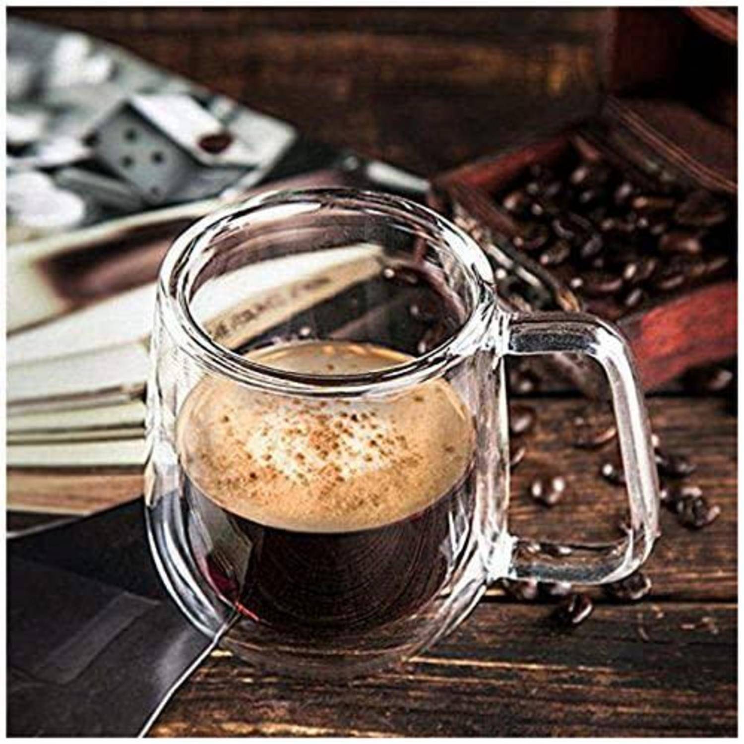 Glastasse mit Espresso auf einem Holztisch, mit verstreuten Kaffeebohnen und einem rustikalen Kaffee-Accessoire im Hintergrund.