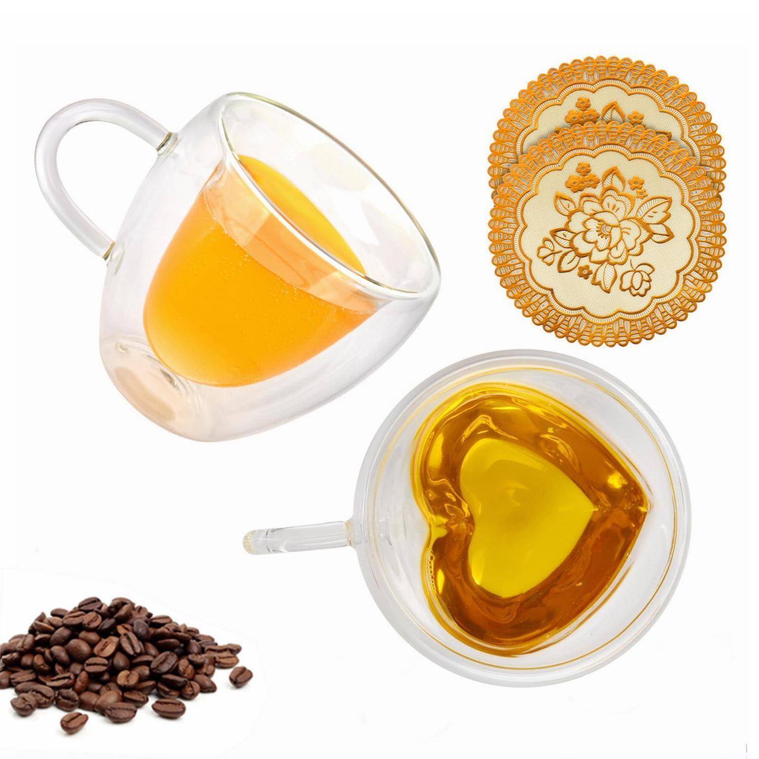 Zwei durchsichtige Glastassen mit bernsteinfarbenen Tee, eine dekorative Teeuntersetzer und ein kleiner Haufen Kaffeebohnen auf weißem Hintergrund.