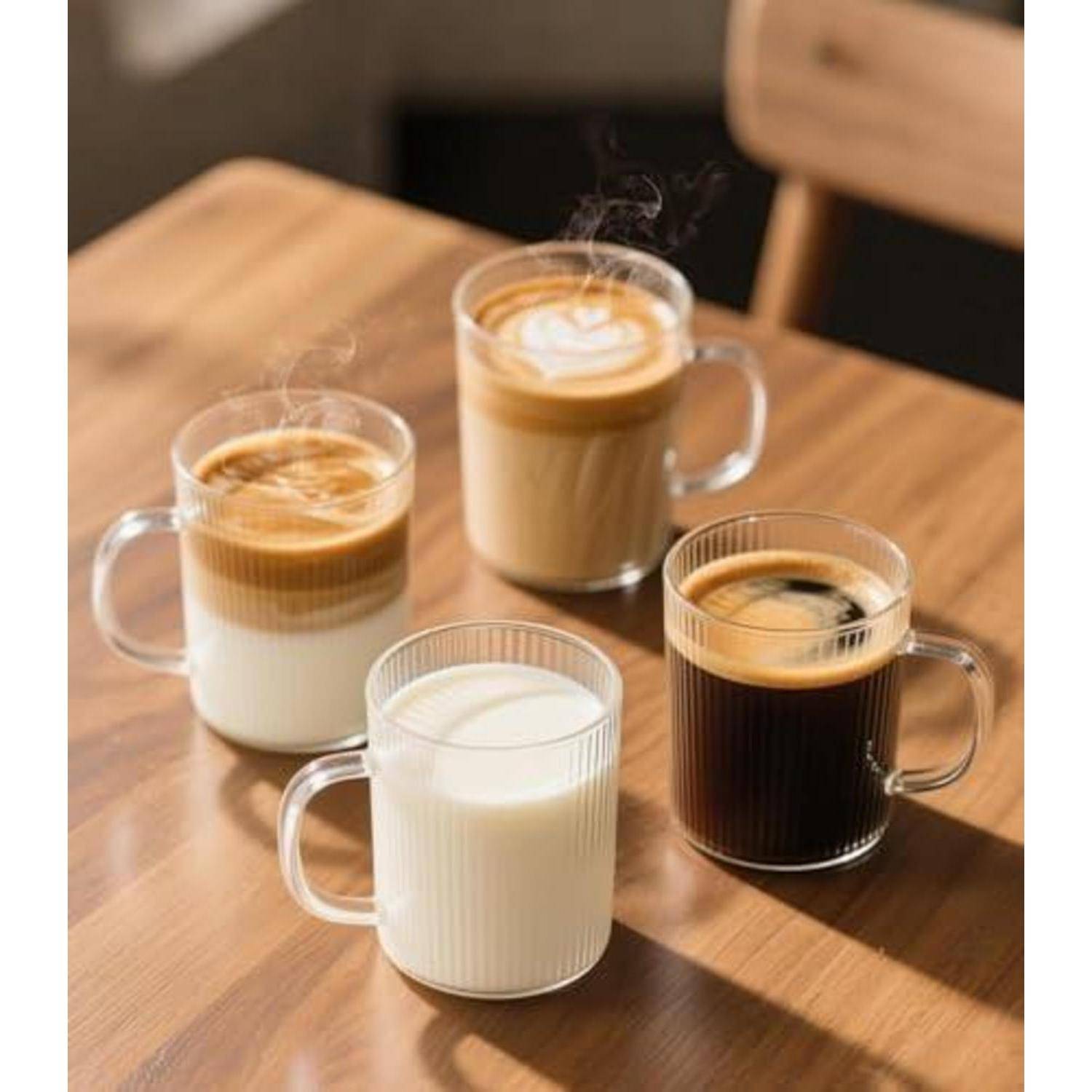 Vier Glastassen mit Kaffeegetränken auf einem Holztisch, darunter Latte, Cappuccino, schwarzer Kaffee und Milch.