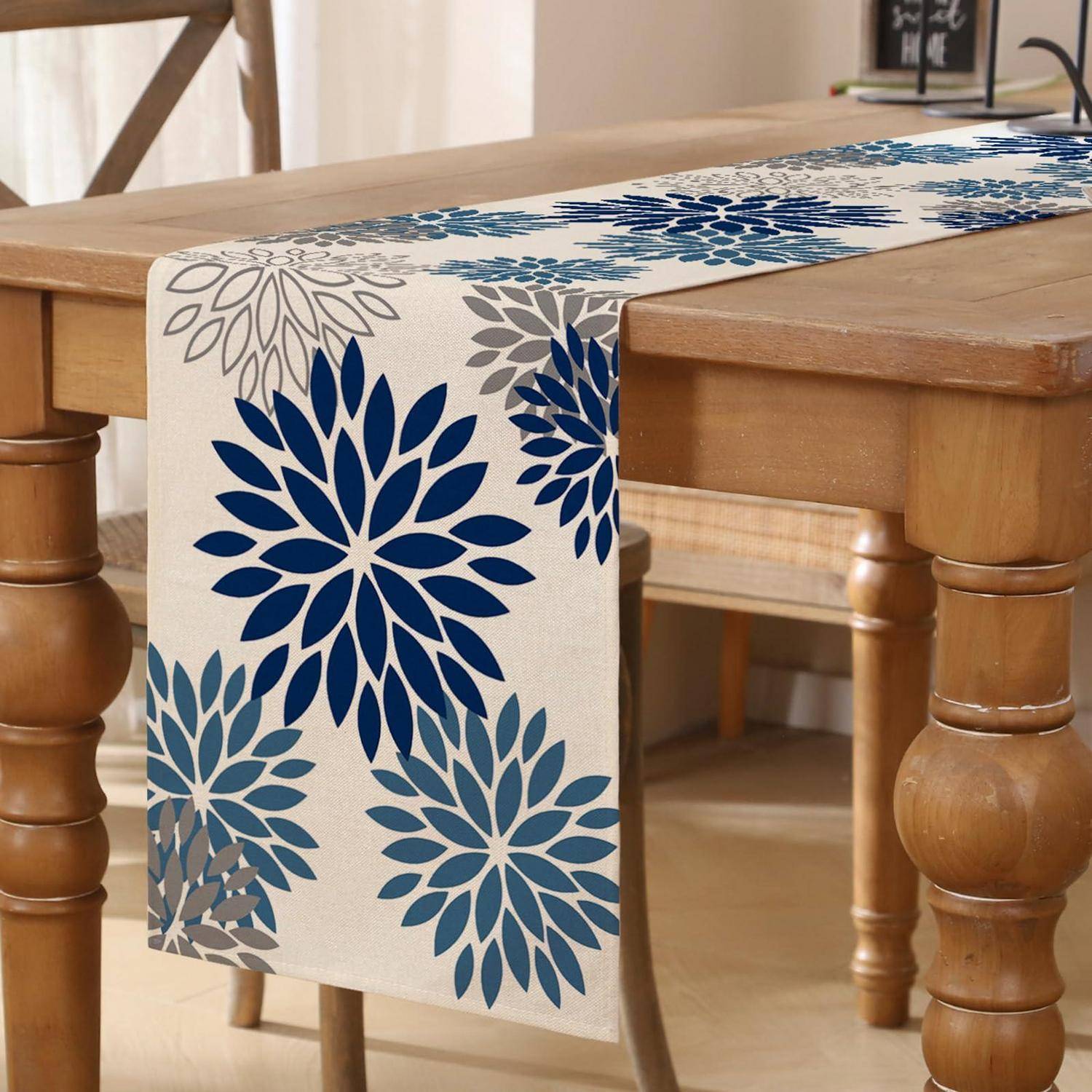 Blauer Tischläufer mit Blumenmuster, über einem Holzesstisch drapiert, mit passenden Platzdeckchen oder Läufern im Hintergrund.