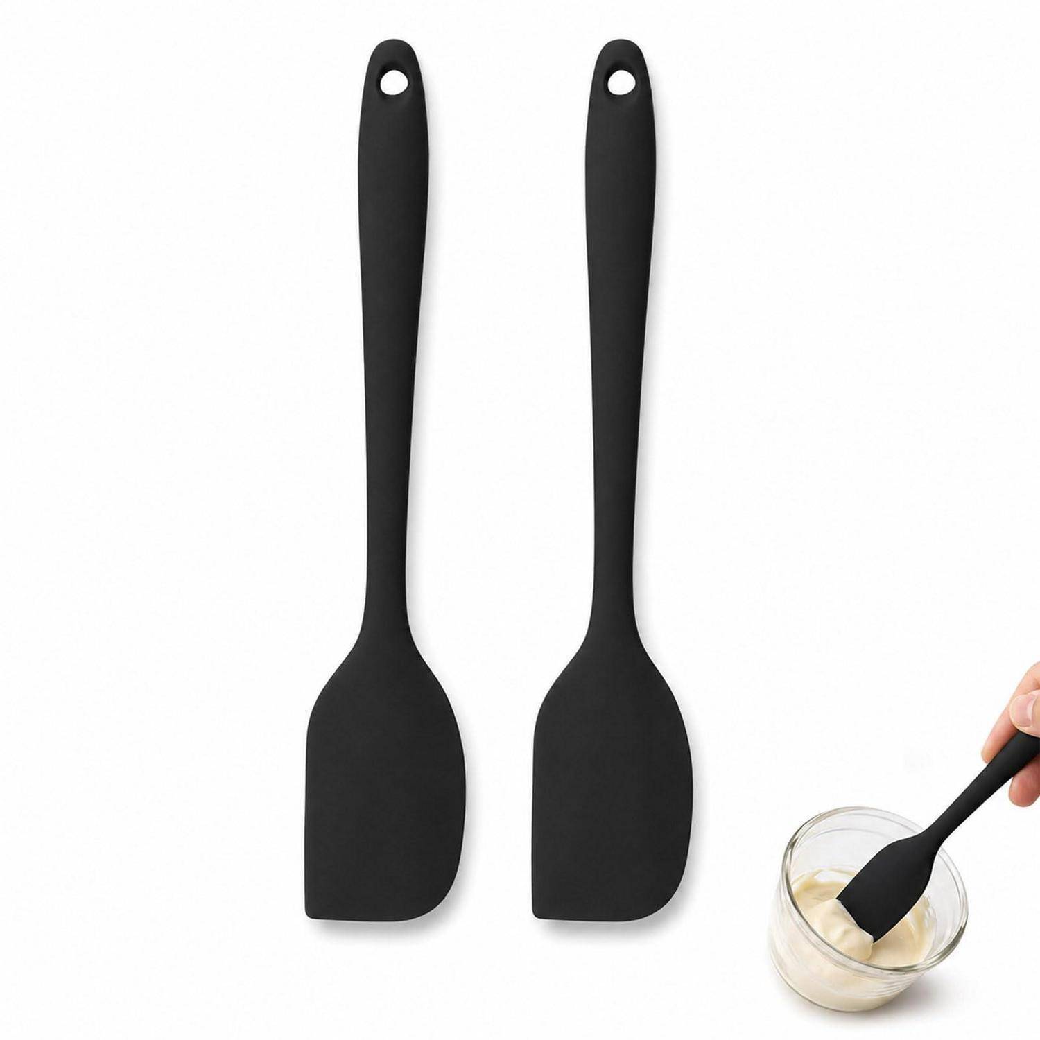 Zwei schwarze Silikonspatel mit Aufhängelöchern, plus ein Handgriff, der einen in eine kleine Schüssel mit Teig oder Sauce auf weißem Hintergrund taucht.