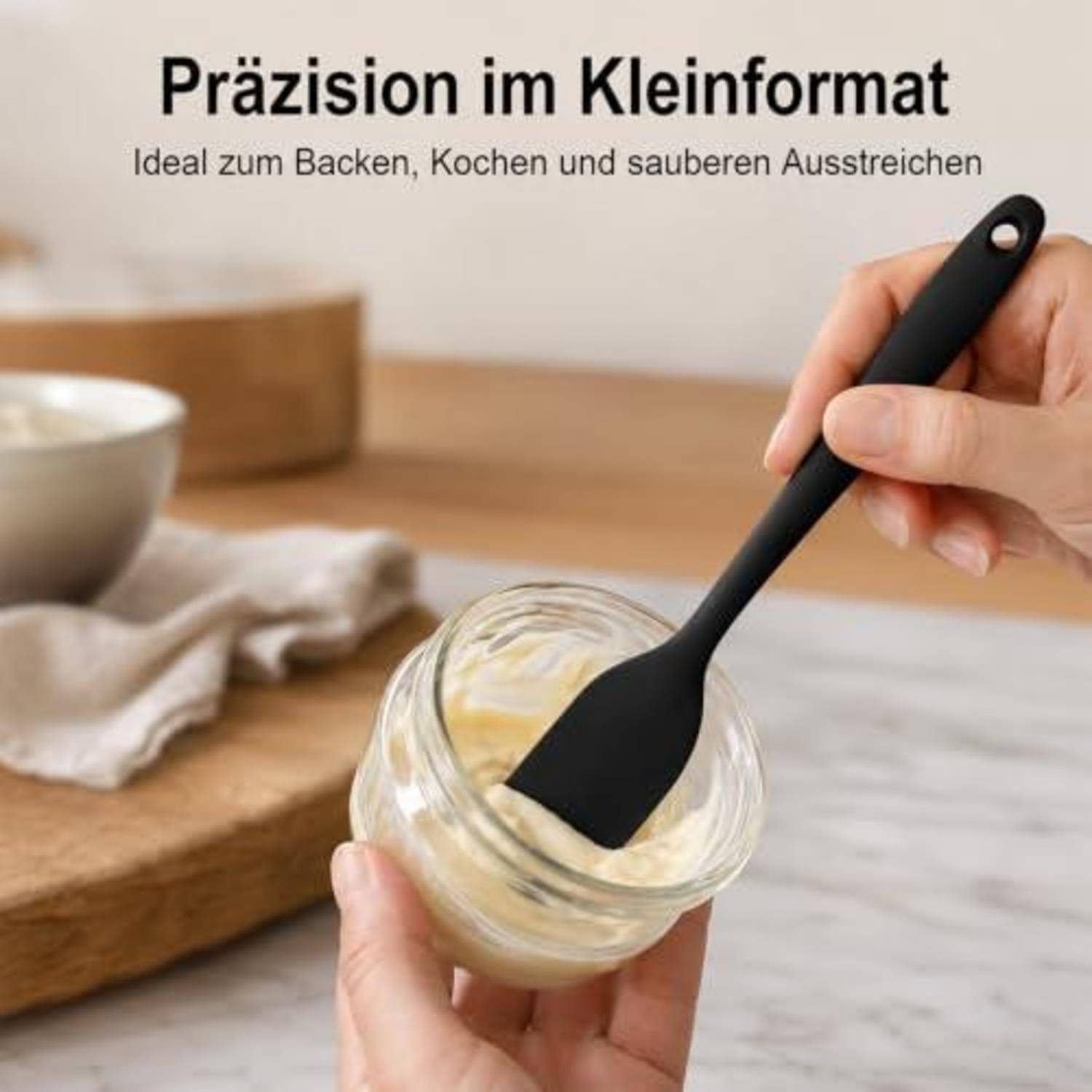 Hände verwenden einen kleinen schwarzen Spachtel zum Abkratzen einer cremigen Mischung aus einem Glas; deutscher Text lautet „Präzision im Kleinformat