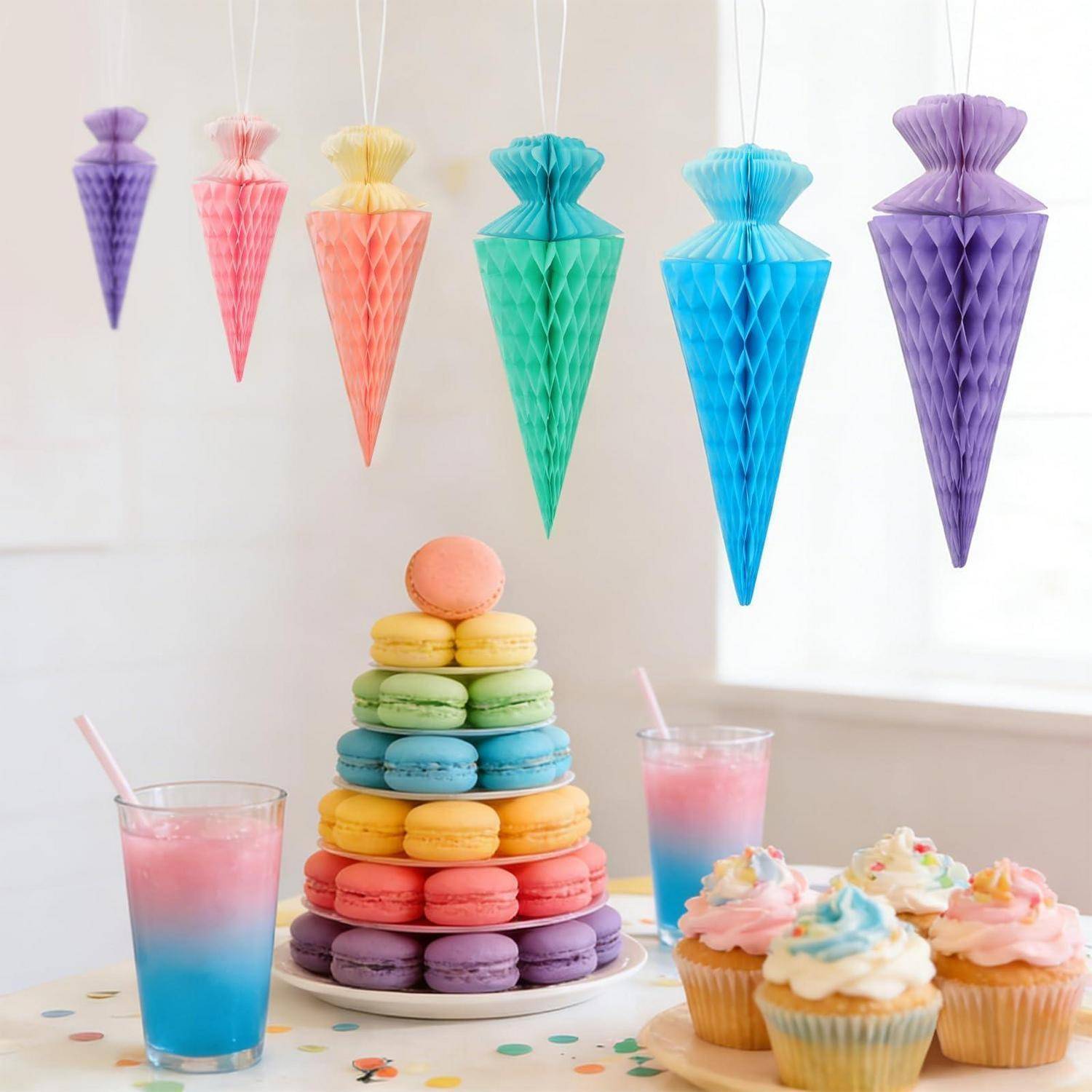 Bunte Desserttafel mit regenbogenfarbenen Makronen, die pyramidenförmig gestapelt sind, Cupcakes in Pastelltönen und rosa-blaue Getränke, dekoriert mit hängenden Papierlaternen.